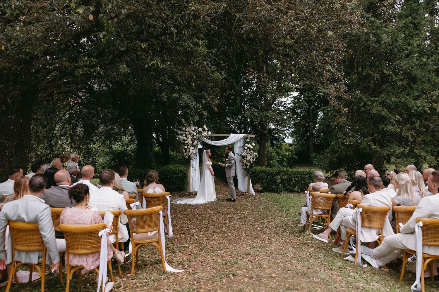 Outdoor wedding ceremony seating arrangement with white chairs facing an altar in a garden.