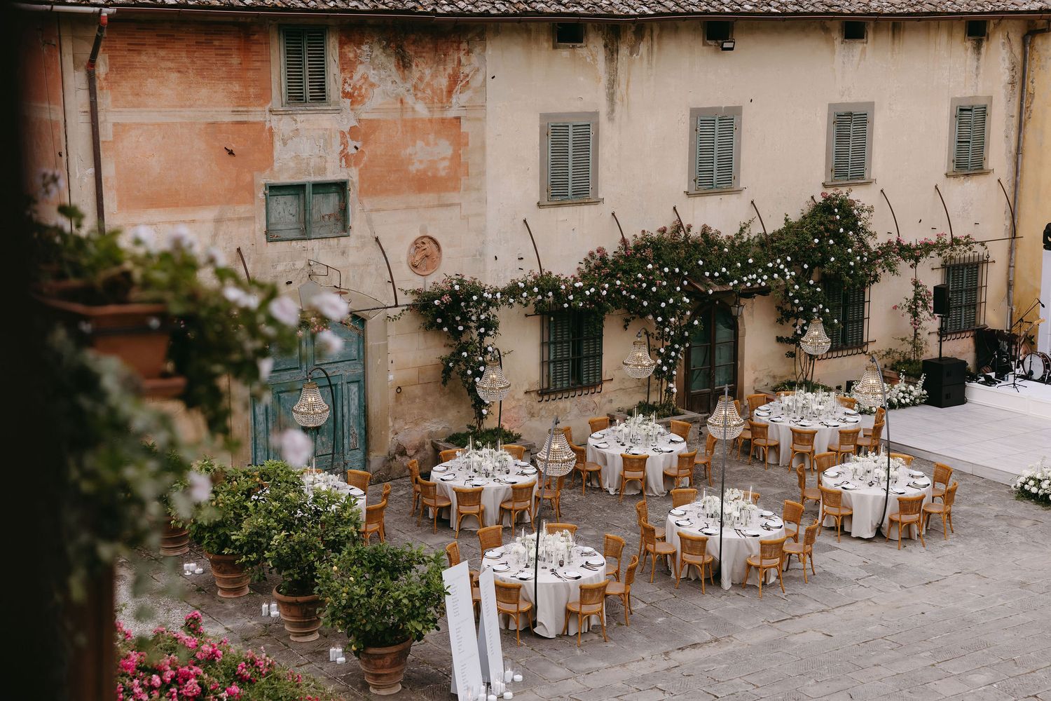 Rustic Italian courtyard set up for an elegant outdoor wedding reception with round tables and string lights.