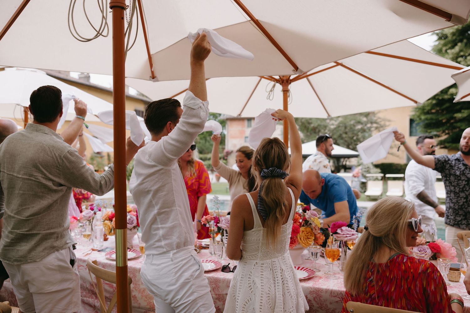 Wedding reception guests seated under white umbrellas at decorated outdoor tables.