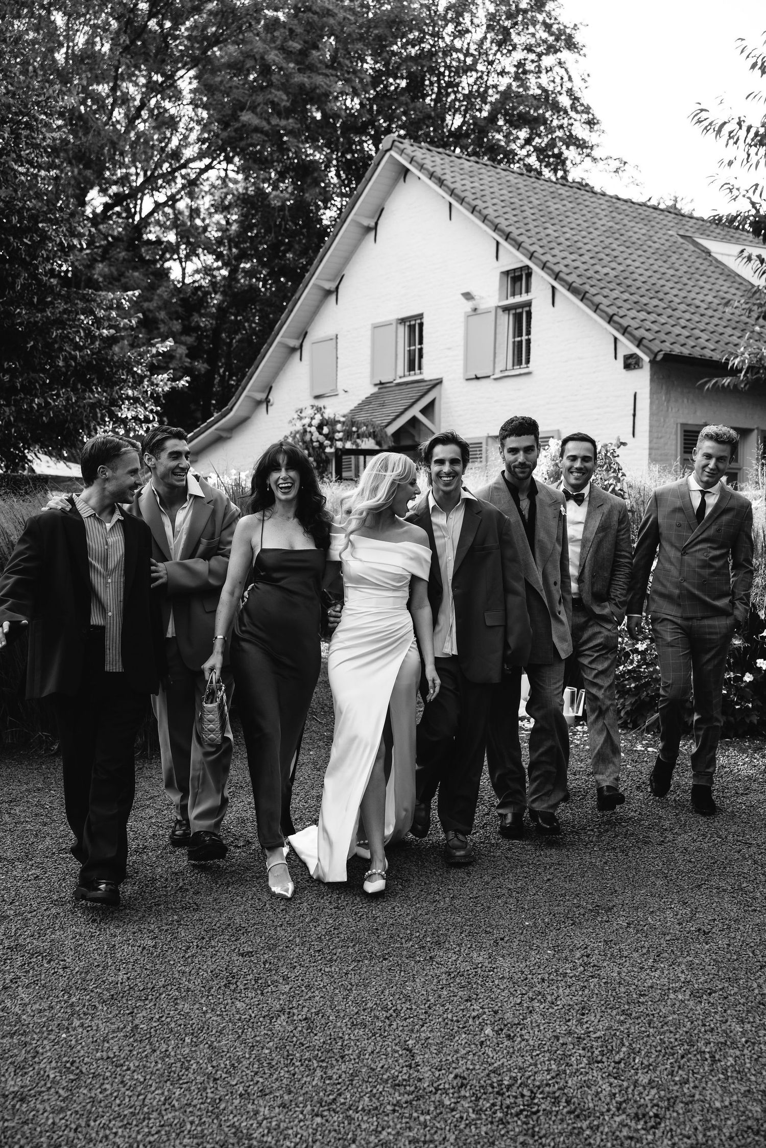 Black and white vintage photo showing a group walking together outdoors by a white house in formal attire.