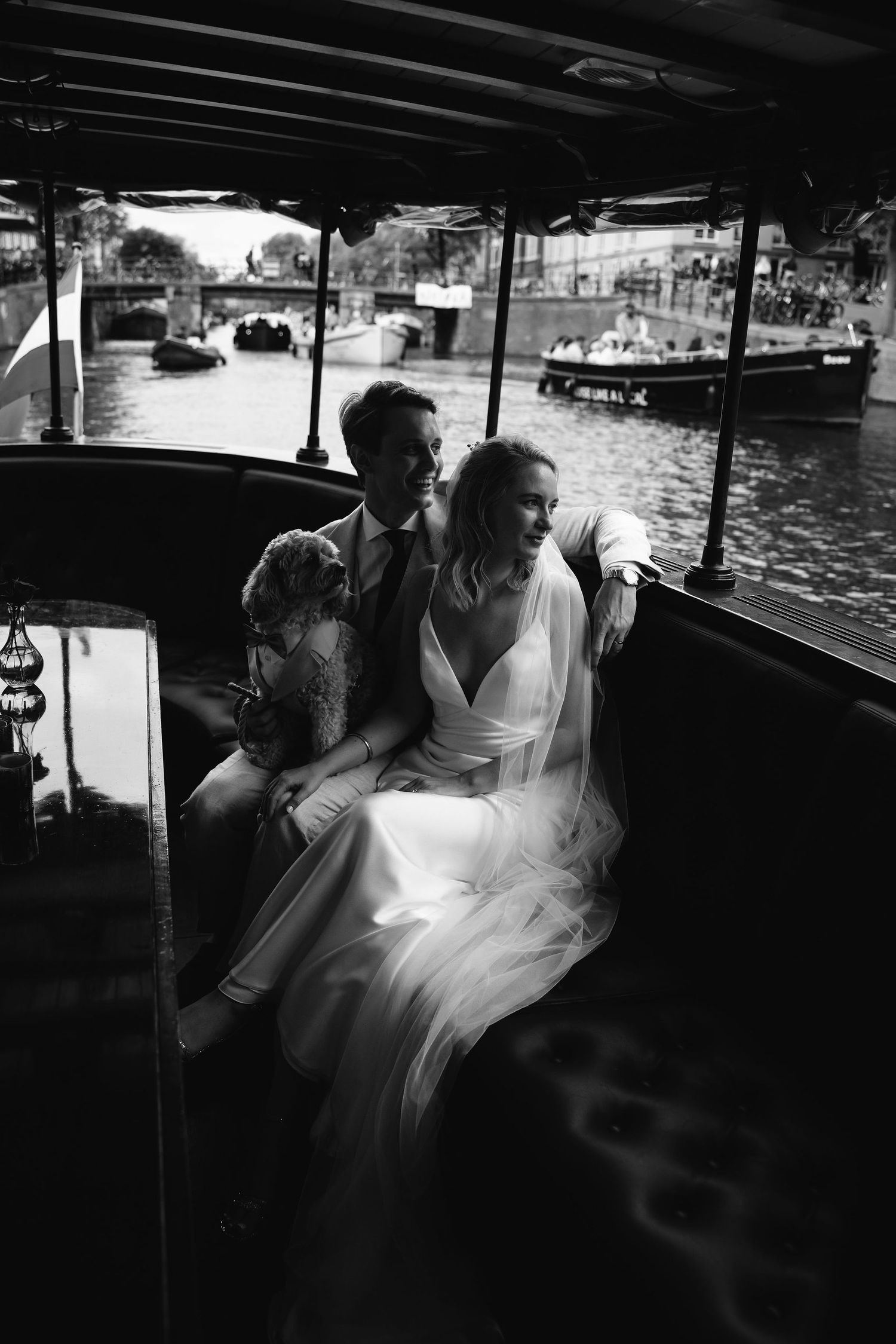 A couple sits together on a boat in black and white, with water and other vessels visible in the background.