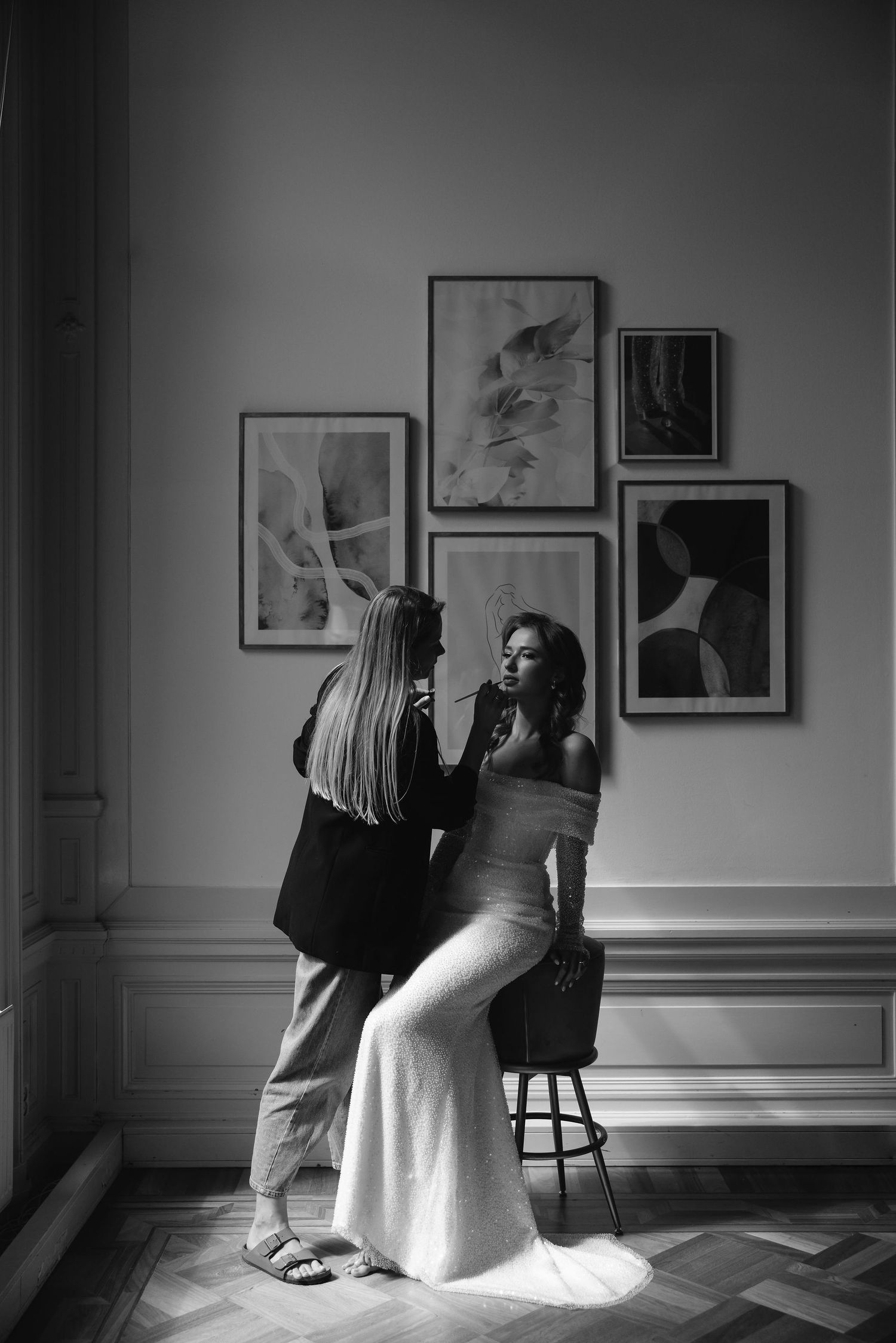 Black and white photo of pre-wedding preparations in an elegant room with framed artwork.