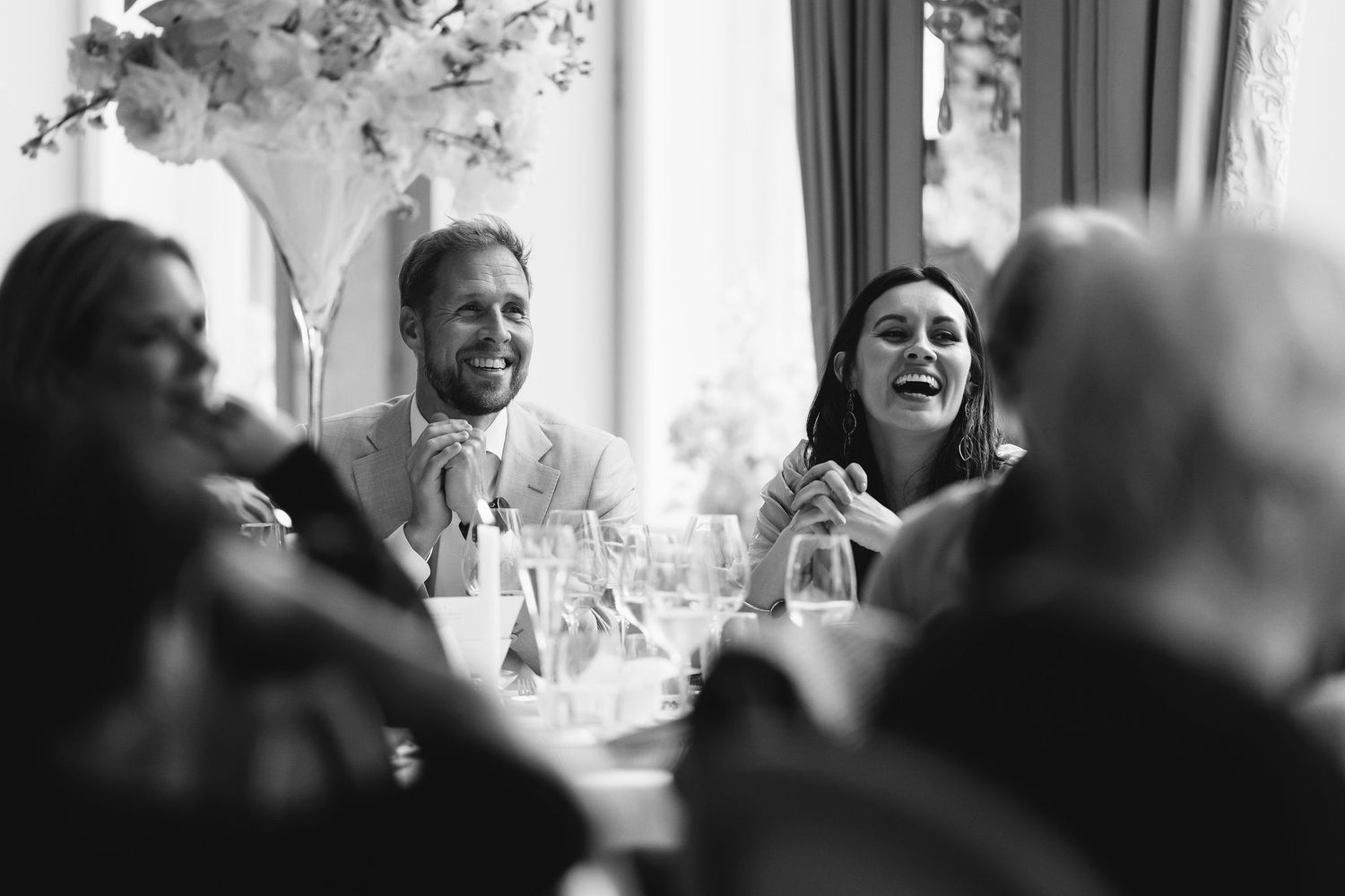Black and white photo of guests laughing during wedding reception.
