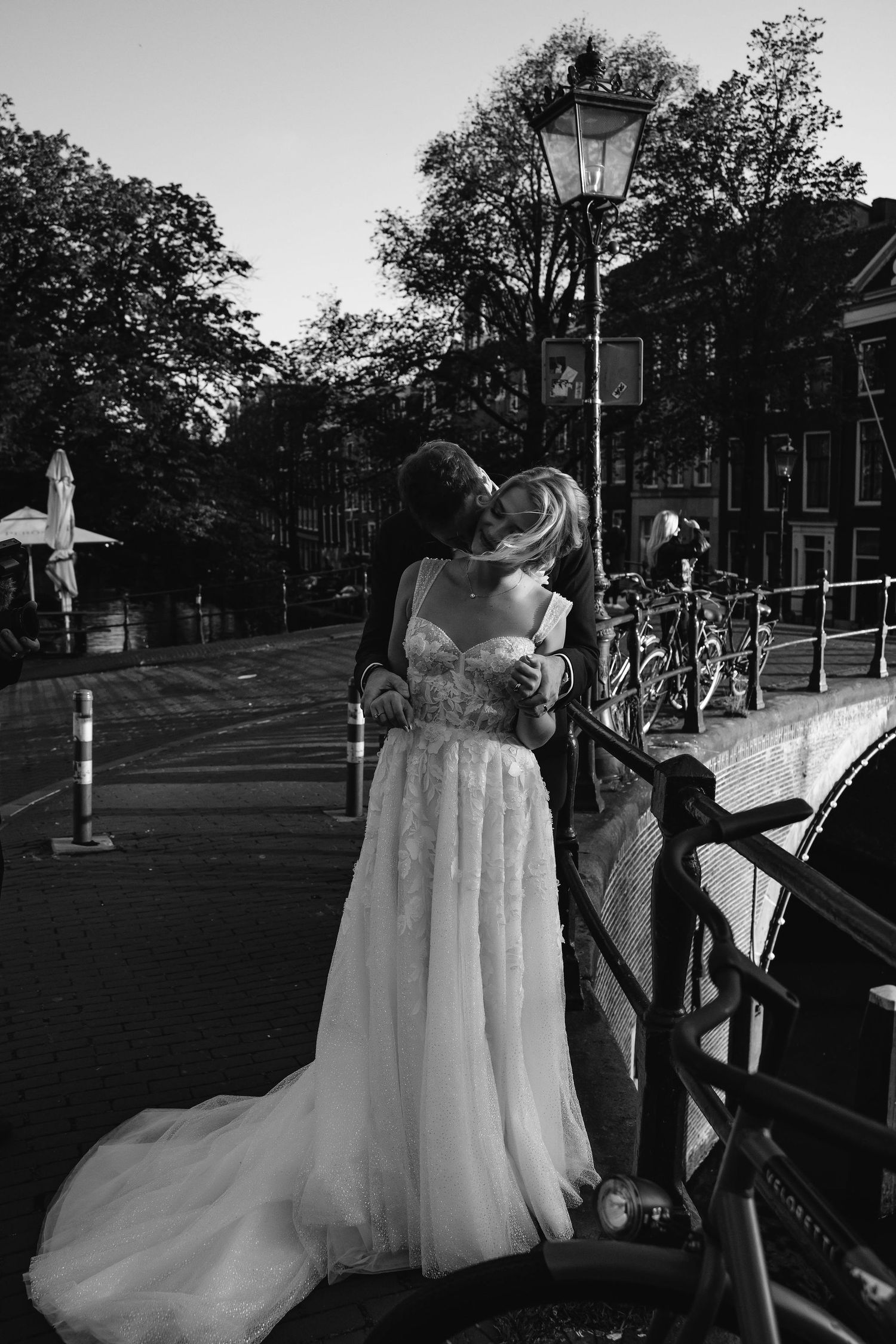 Elegantly dressed couple photographed in outdoor evening setting with vintage street lamps and trees.