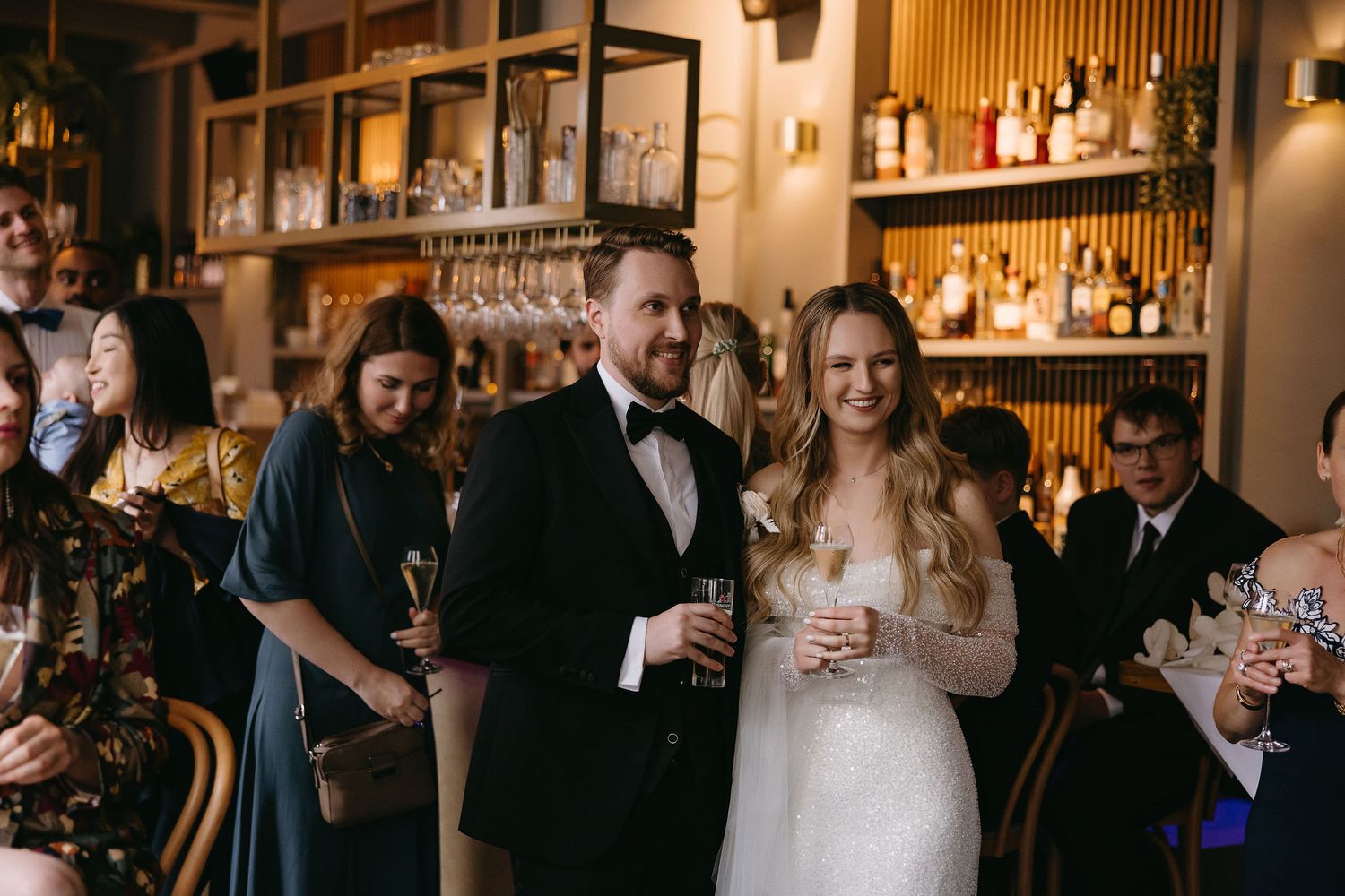 Couple celebrating at wedding reception in elegant bar setting with ambient lighting.