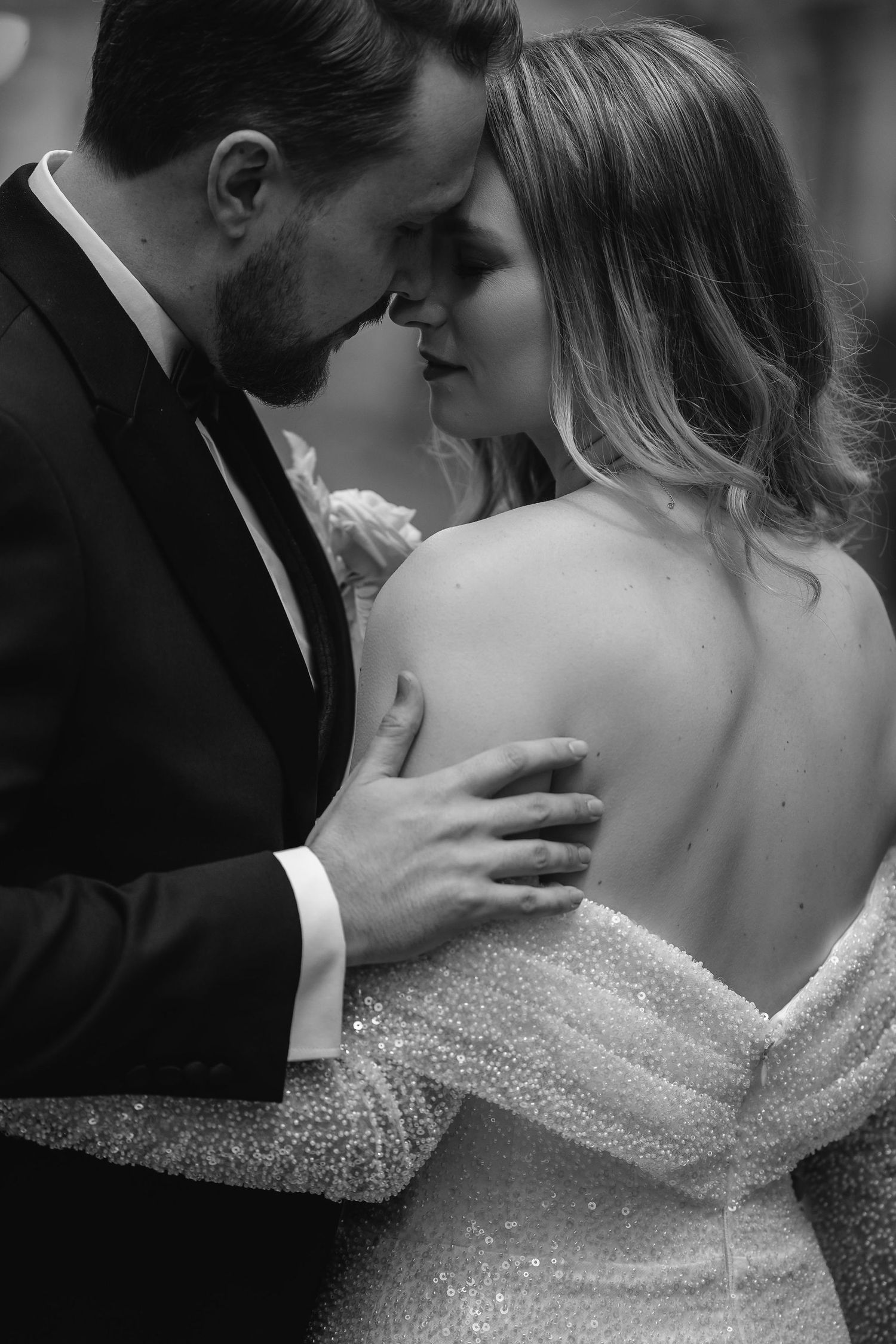 Intimate black and white portrait of newlyweds sharing a tender moment in formal wedding attire.