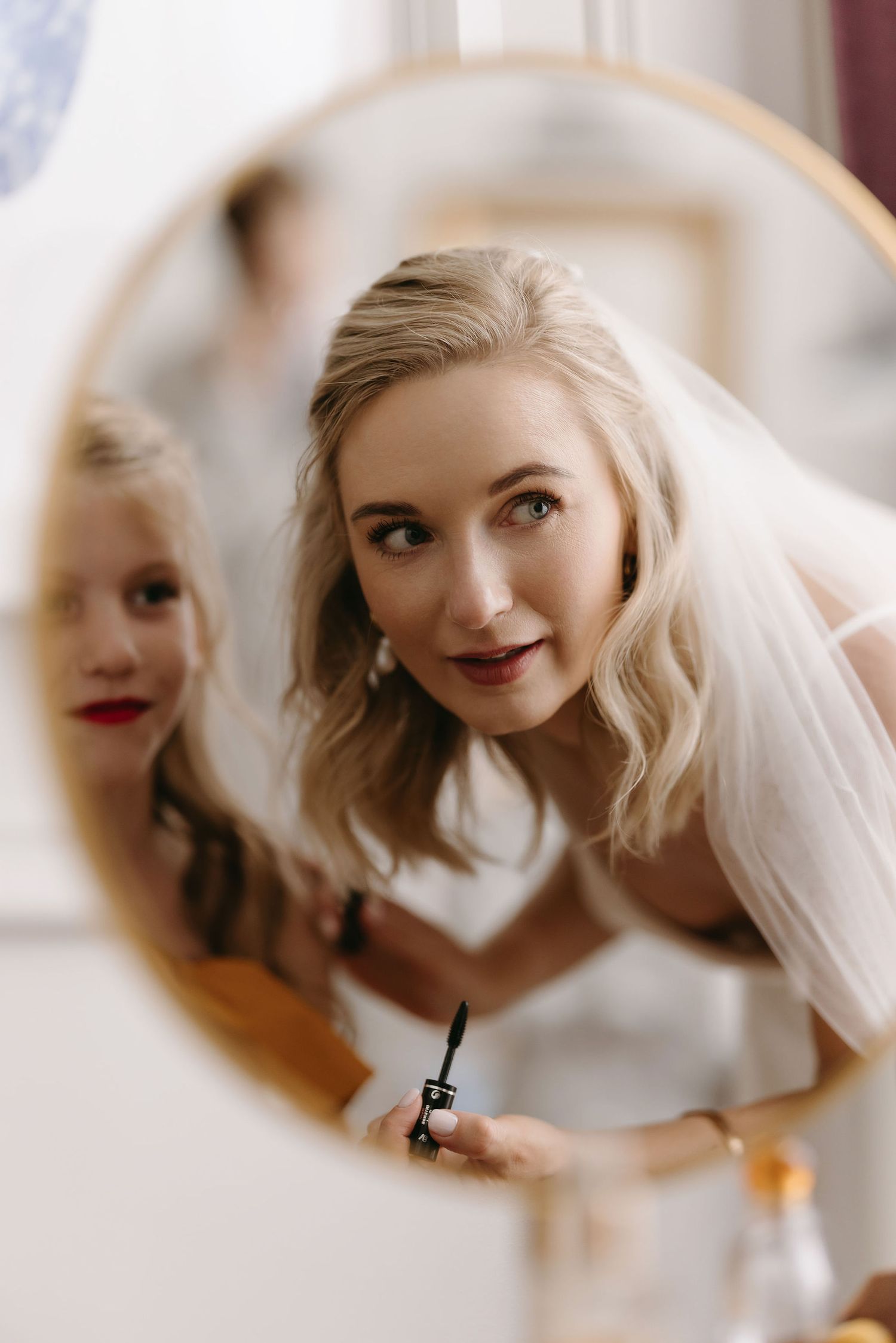 Reflection in round mirror shows wedding preparations with soft natural lighting.