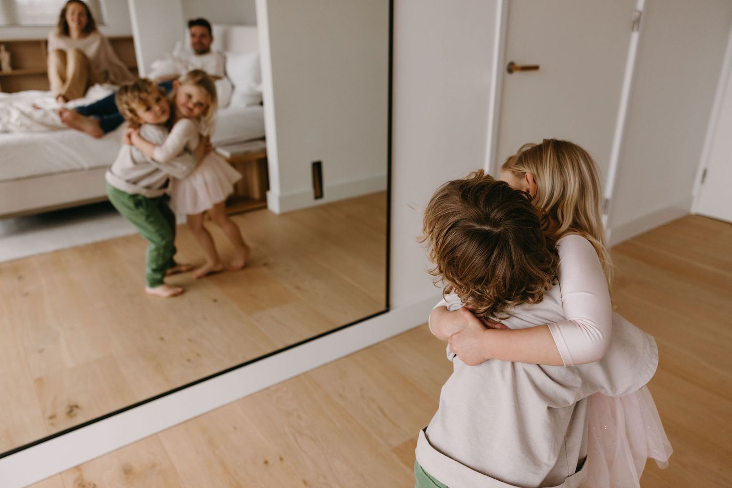 Young children playing and hugging in front of a full-length mirror.