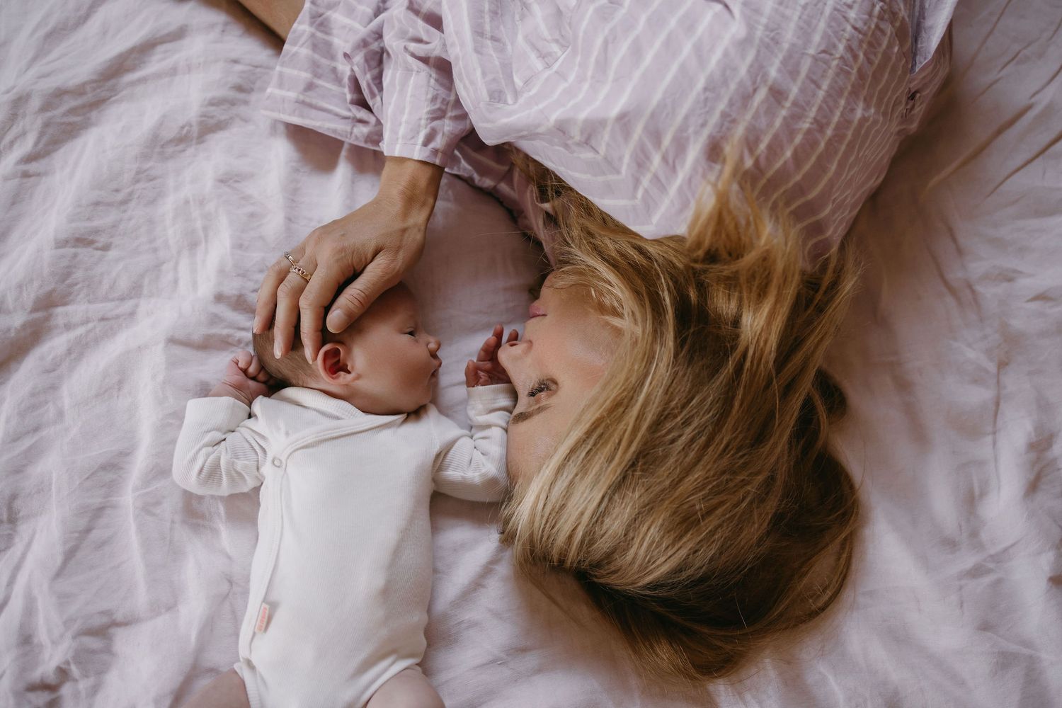 An intimate overhead view of a parent and baby lying together on white bedding.