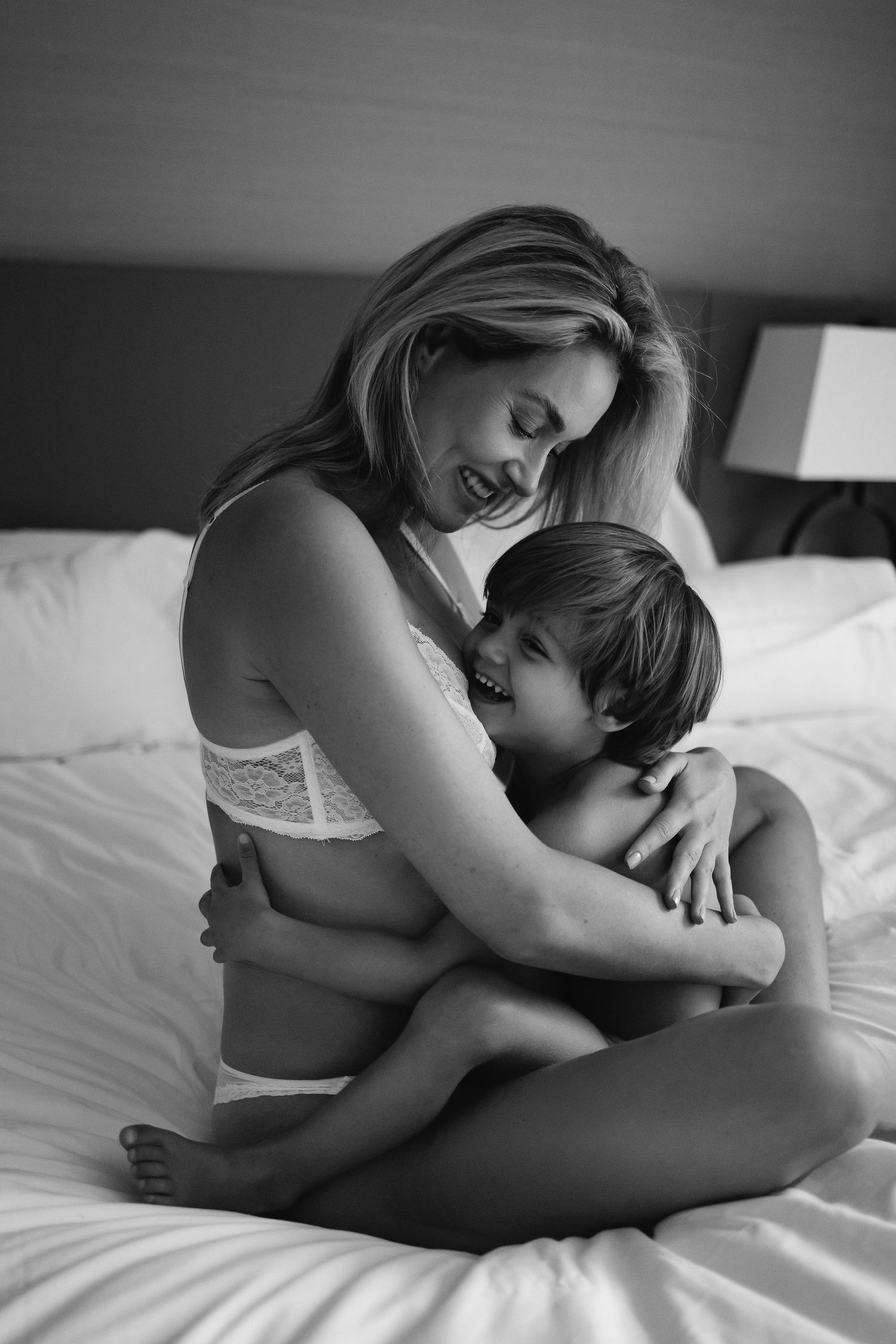 Black and white portrait capturing intimate mother-child moment in white bedding.