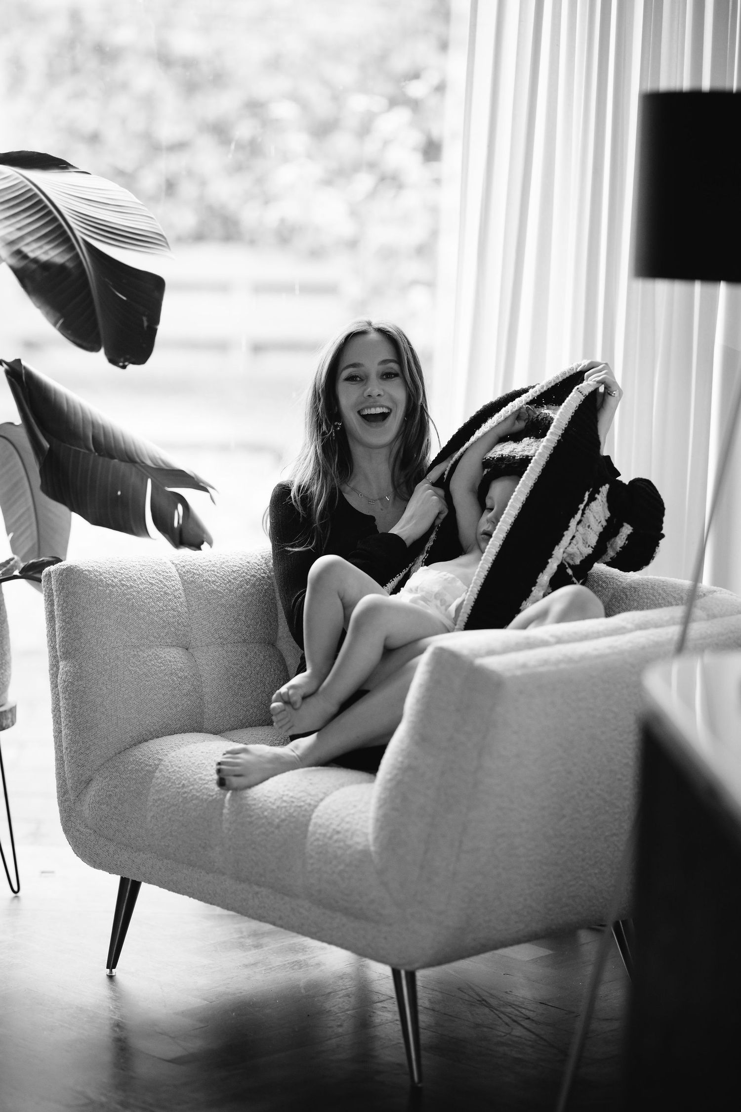 Woman laughs while sitting on modern gray chair during photo session.