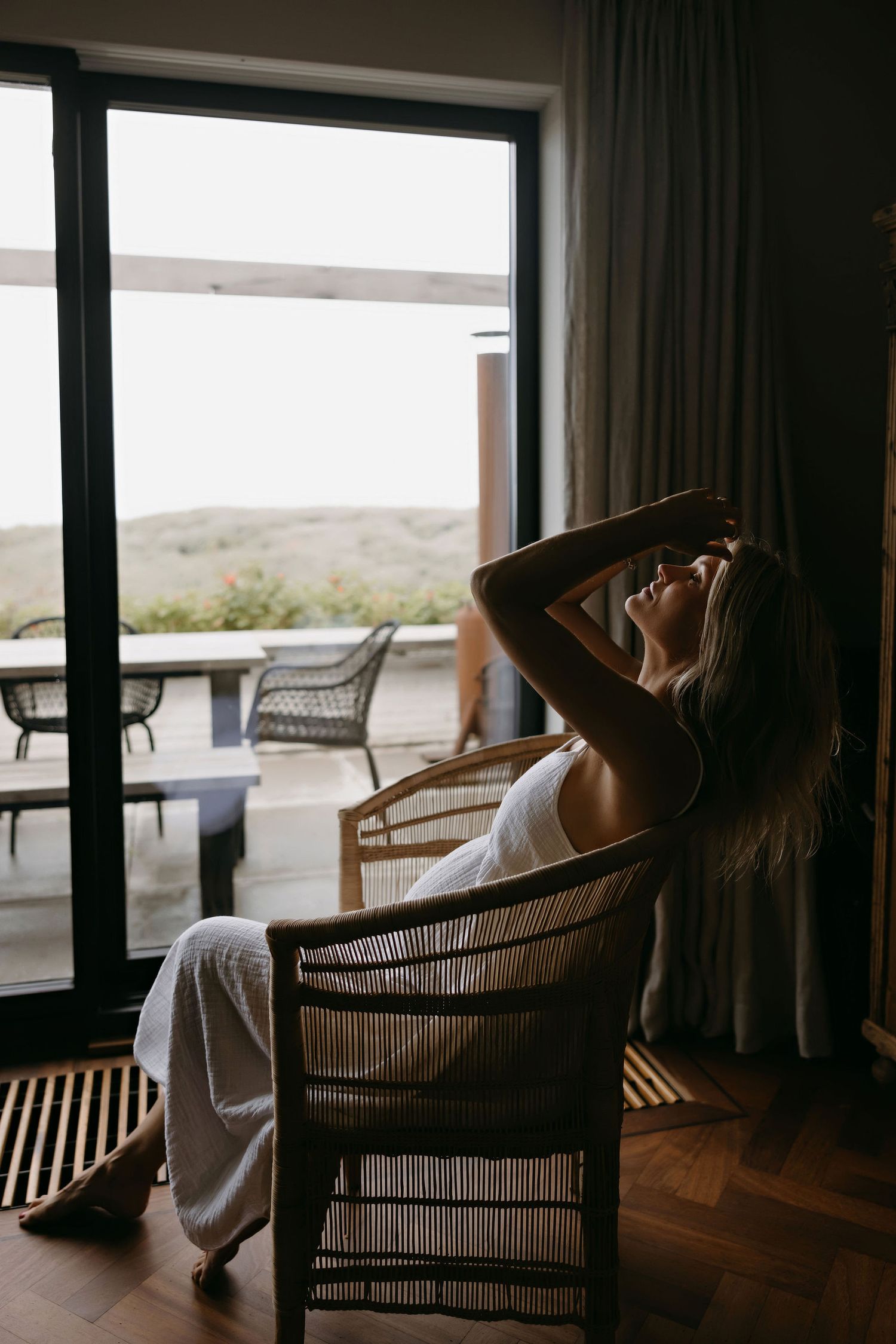 Silhouette of someone relaxing in a wicker chair by a window with scenic outdoor view.
