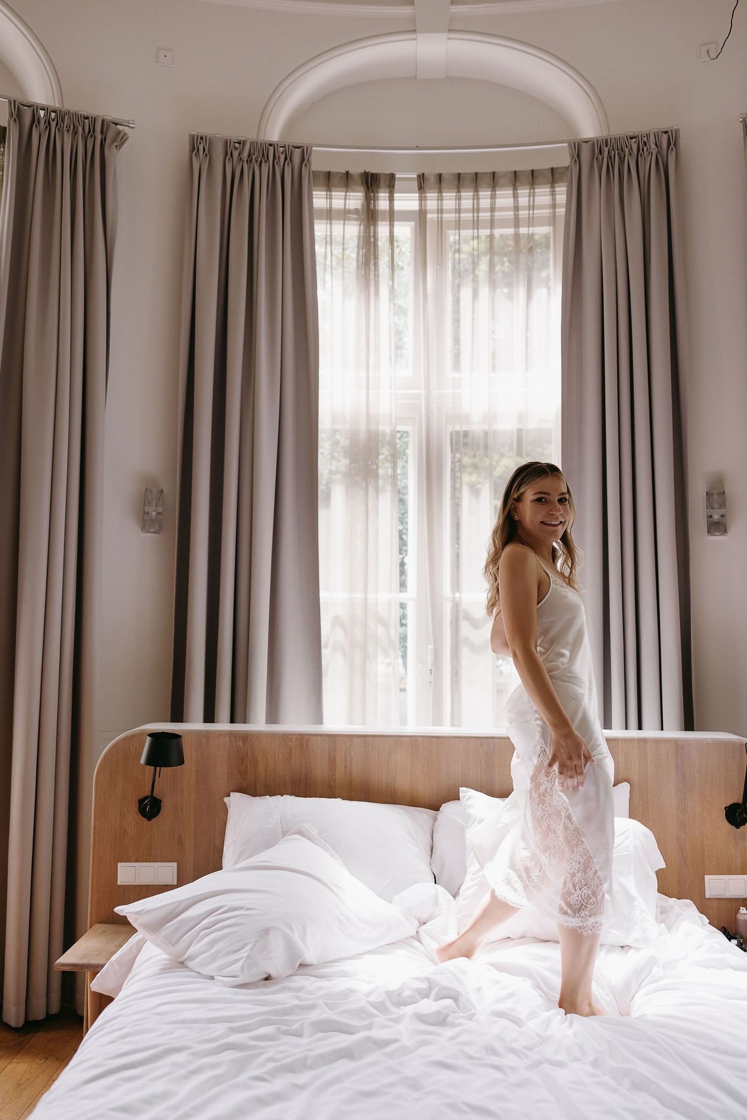 White bedroom interior with bay windows and flowing curtains during bridal preparation.