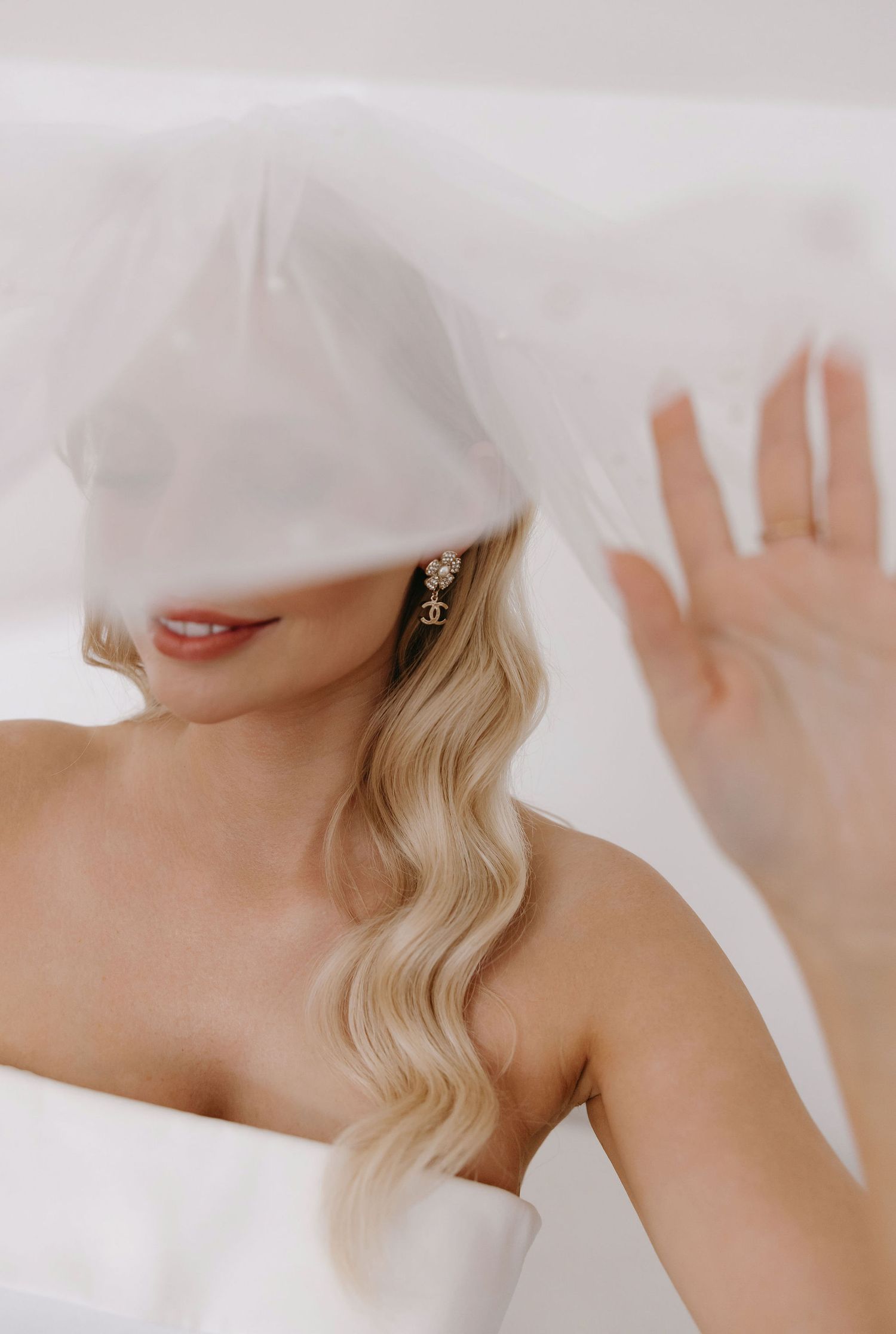Ethereal bridal portrait showing wavy blonde hair and delicate earring under soft white veil.