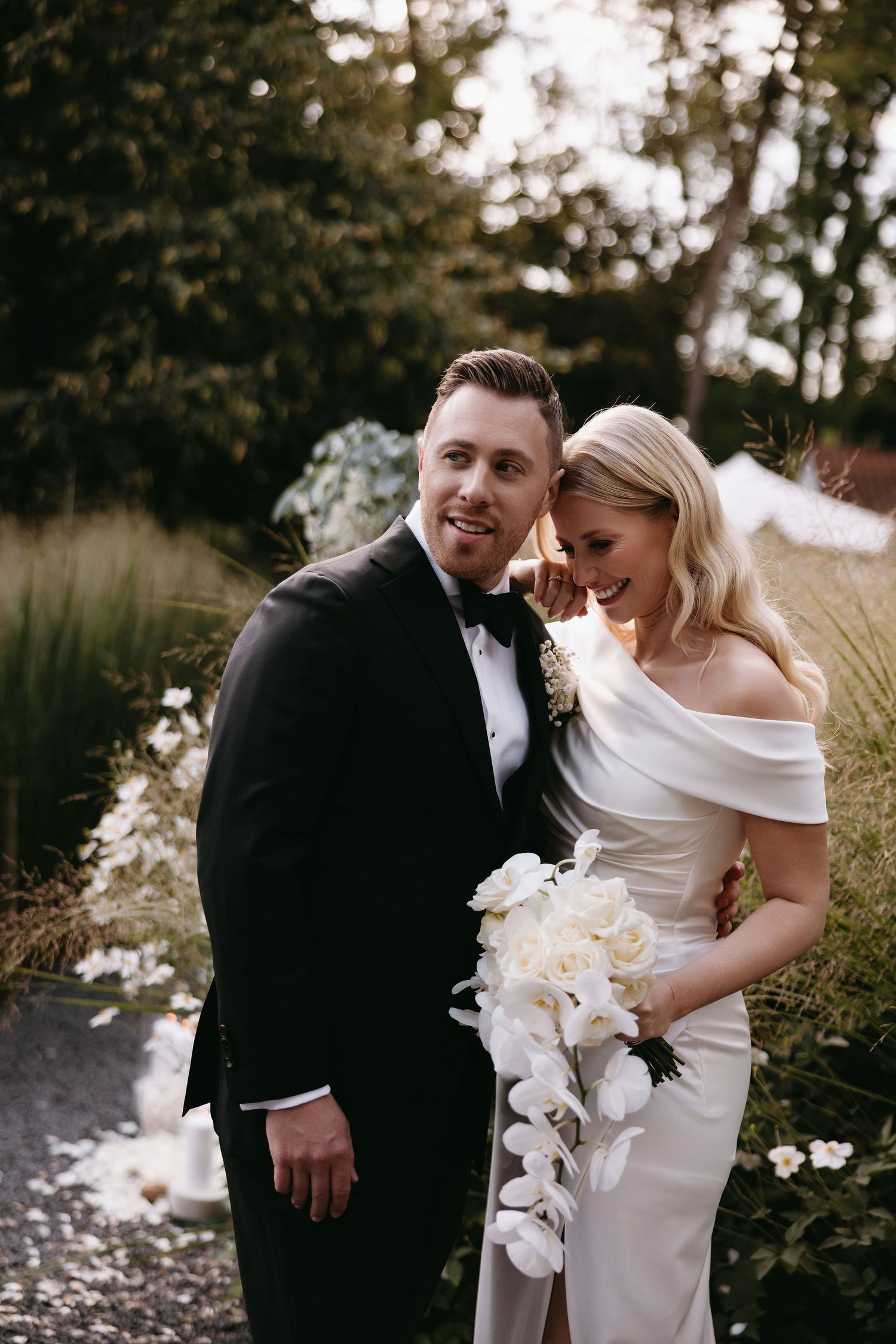 A newlywed couple sharing an intimate moment in their wedding attire against a garden background.