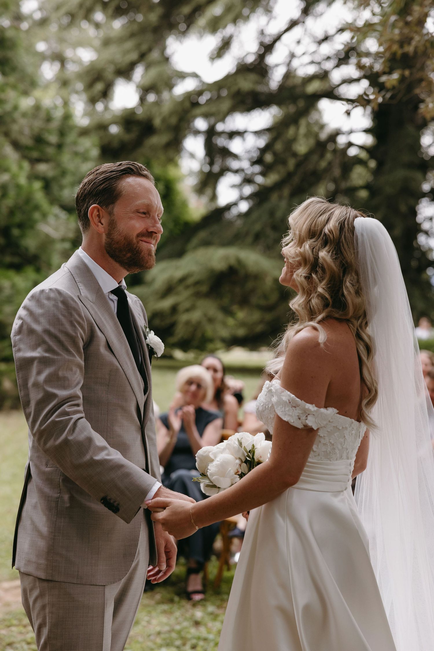 Intimate outdoor wedding ceremony moment between couple in traditional white dress and light gray suit.