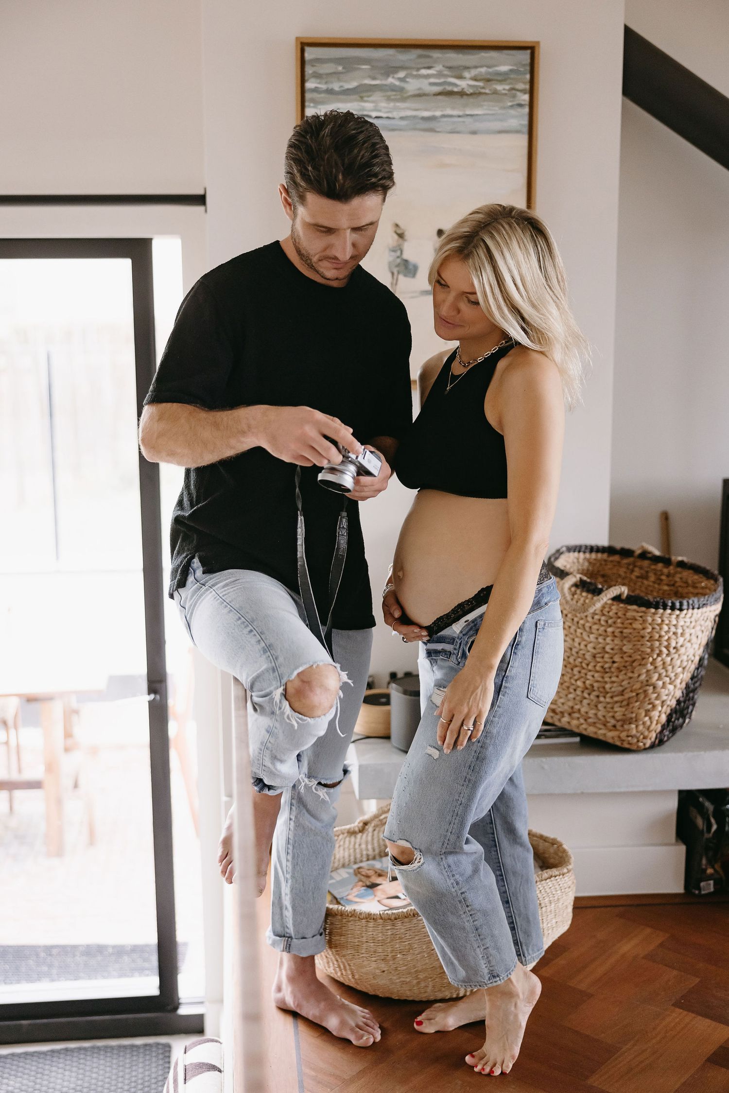 Expecting couple in casual wear sharing an intimate moment while taking photos in their modern home.
