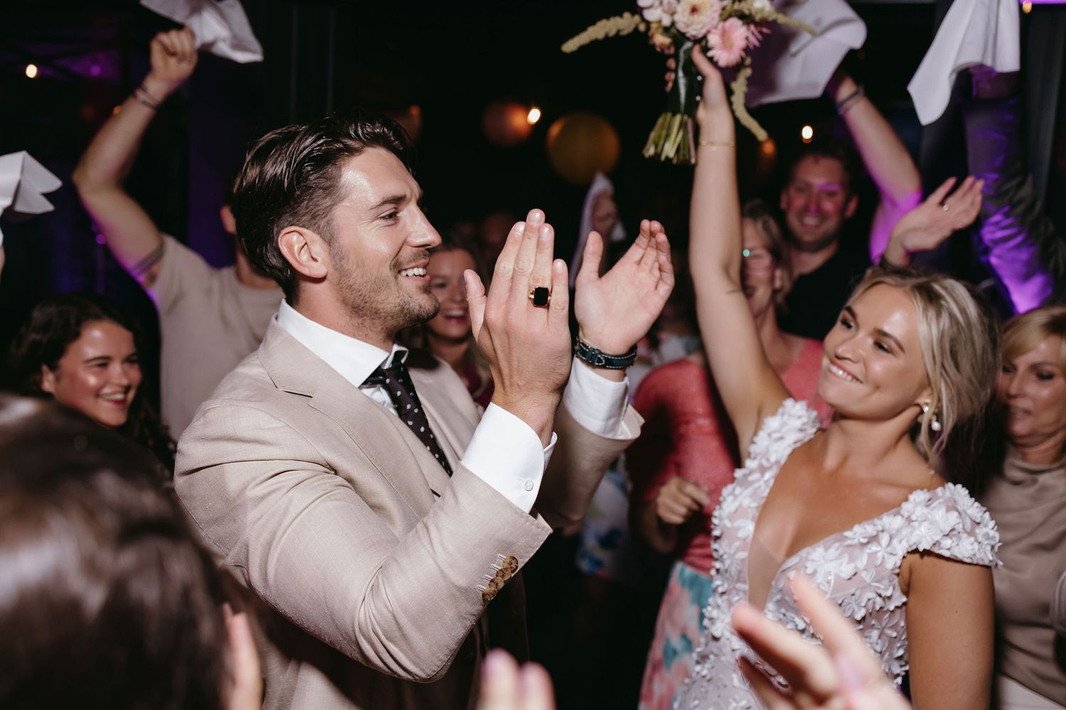 Dancing and celebration at a dimly lit wedding reception with party atmosphere.