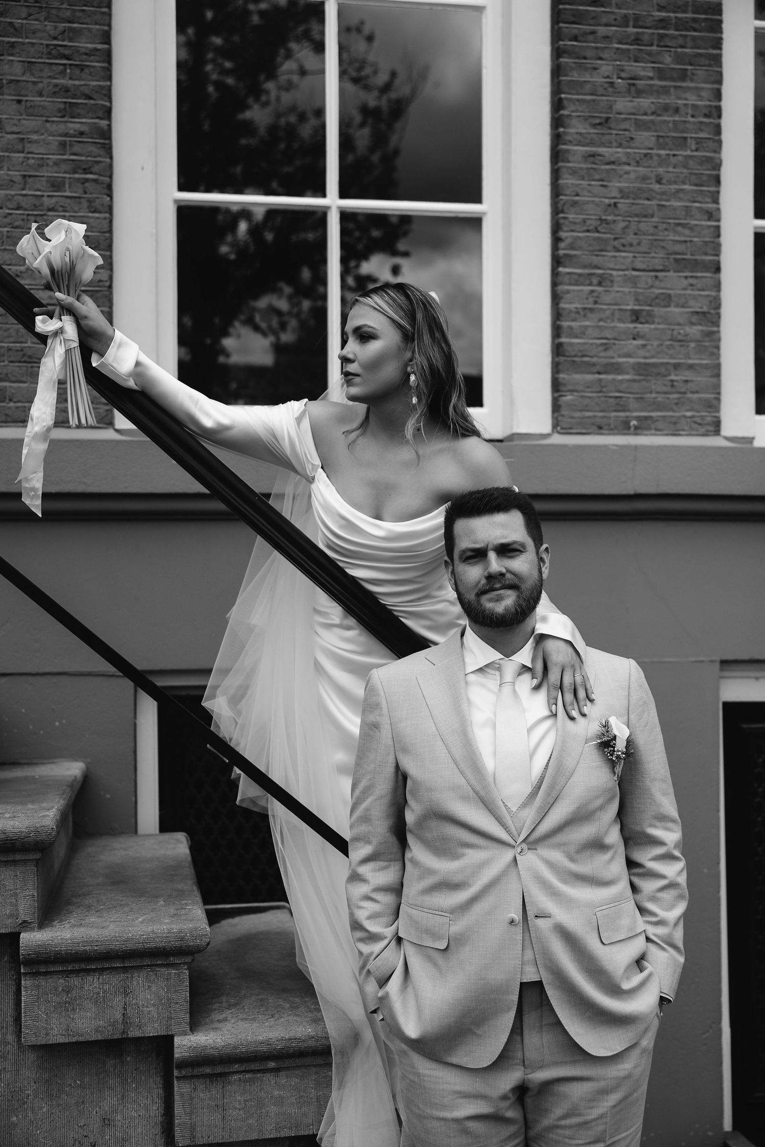Wedding couple poses on historic building steps in black and white, with the bride holding onto a railing.