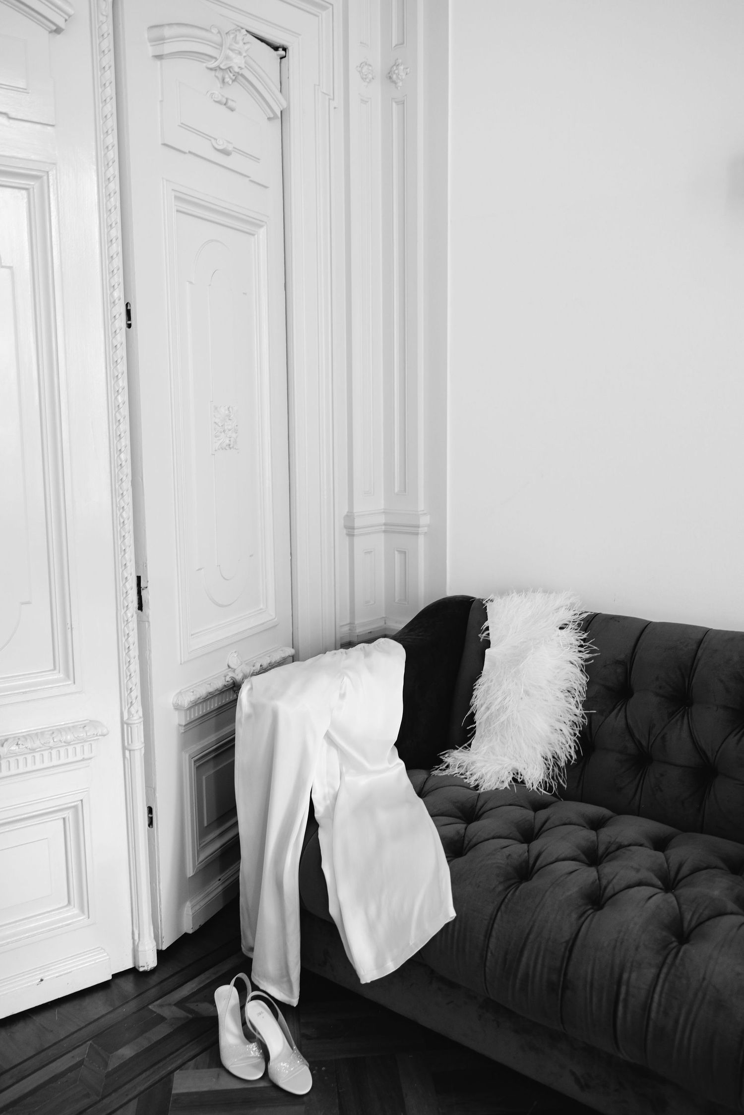 Wedding dress and accessories displayed on black tufted couch in elegant white room.