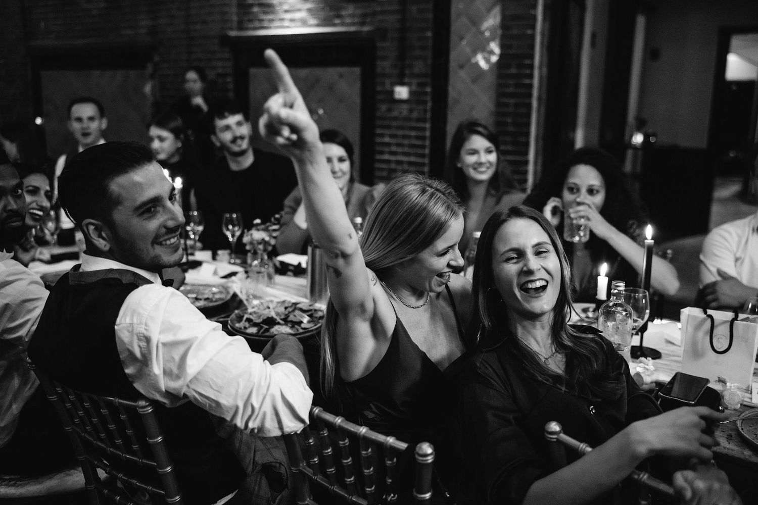 Black and white photo capturing energetic celebrations during a wedding reception dinner.
