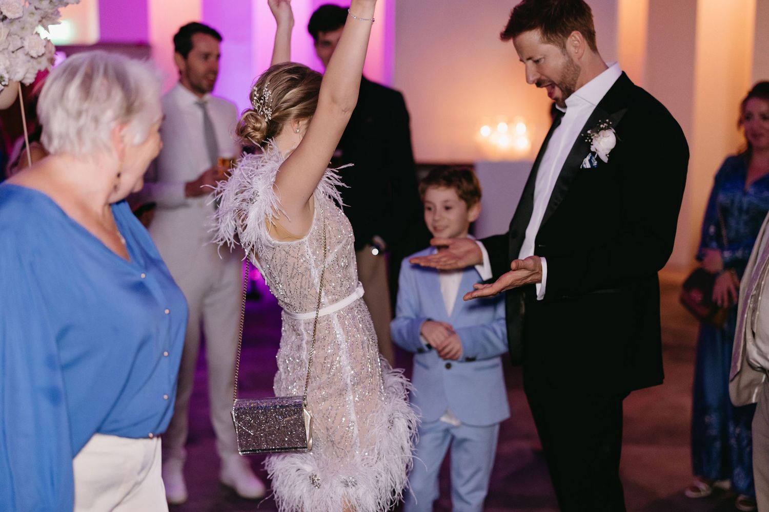 Guests dancing and celebrating at a wedding reception with purple ambient lighting.