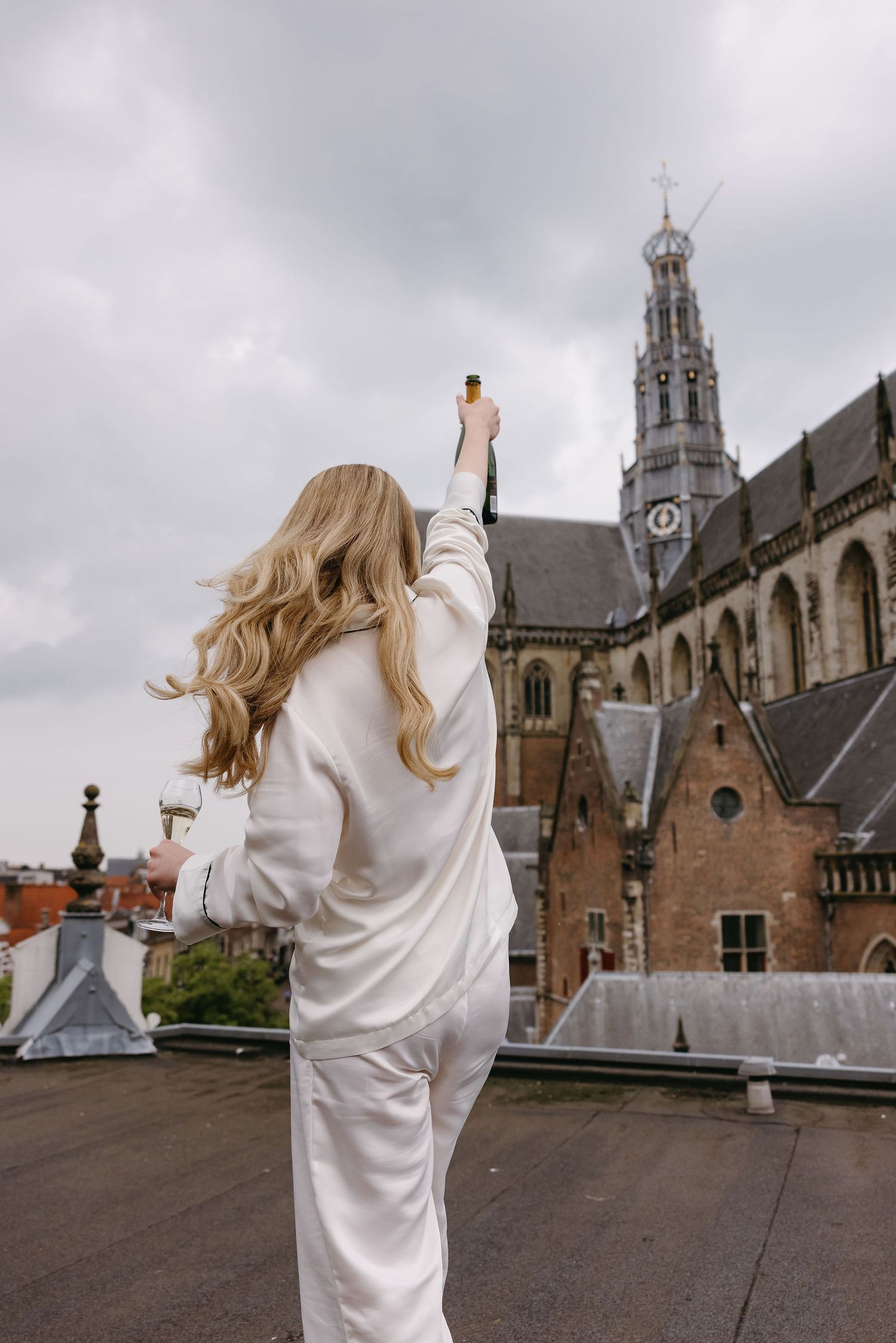Woman in white outfit raises arms triumphantly in front of historic church architecture.