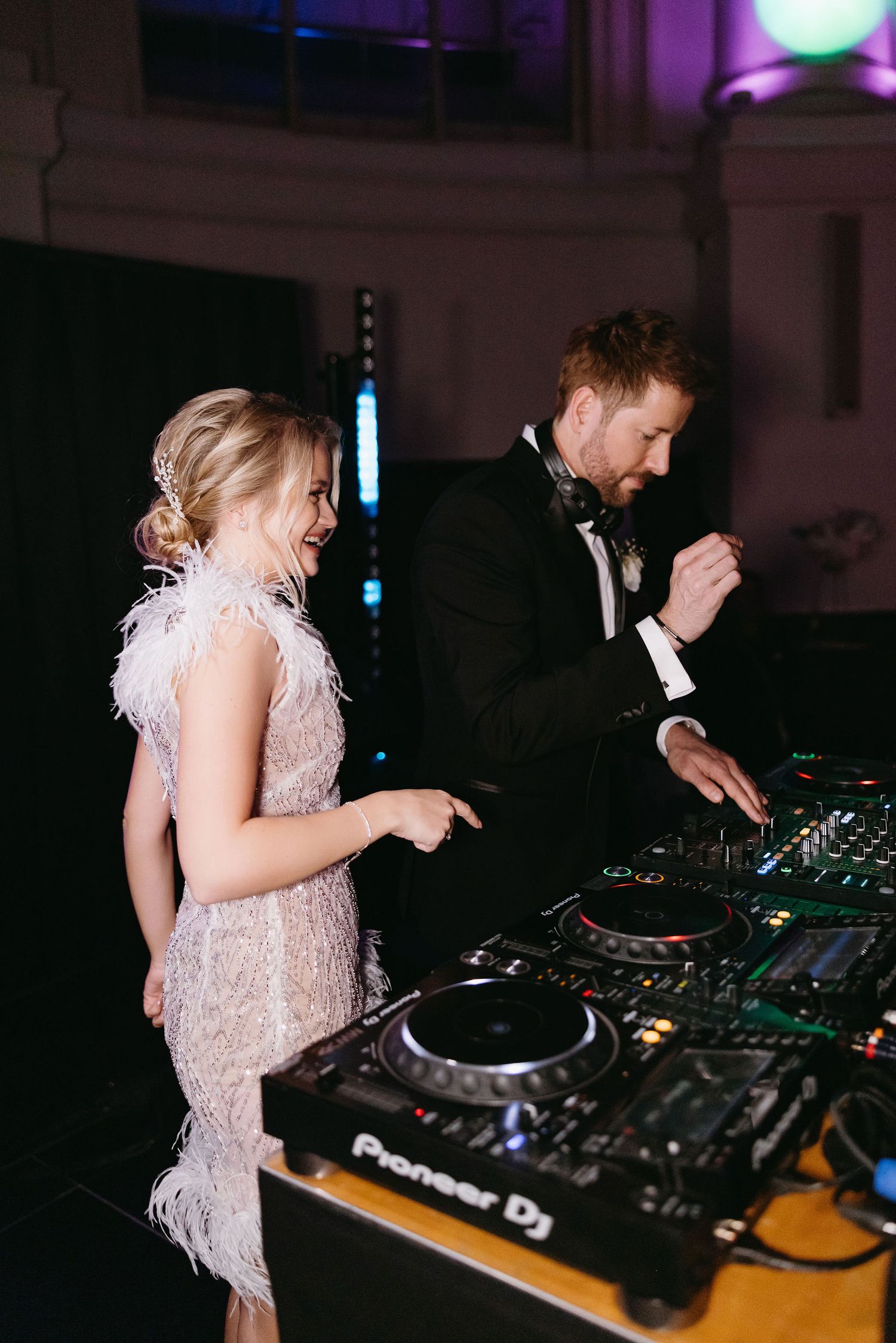 DJ equipment and controllers at night wedding reception with purple lighting.