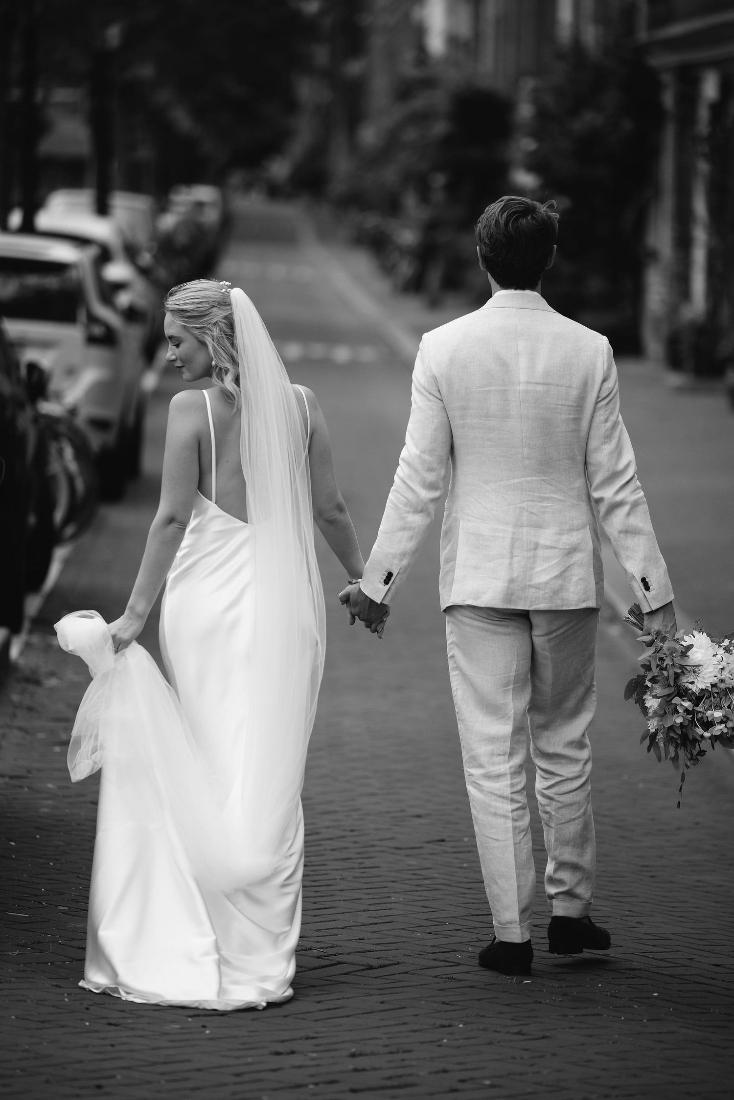 A couple walks hand in hand on cobblestone streets in black and white photography.