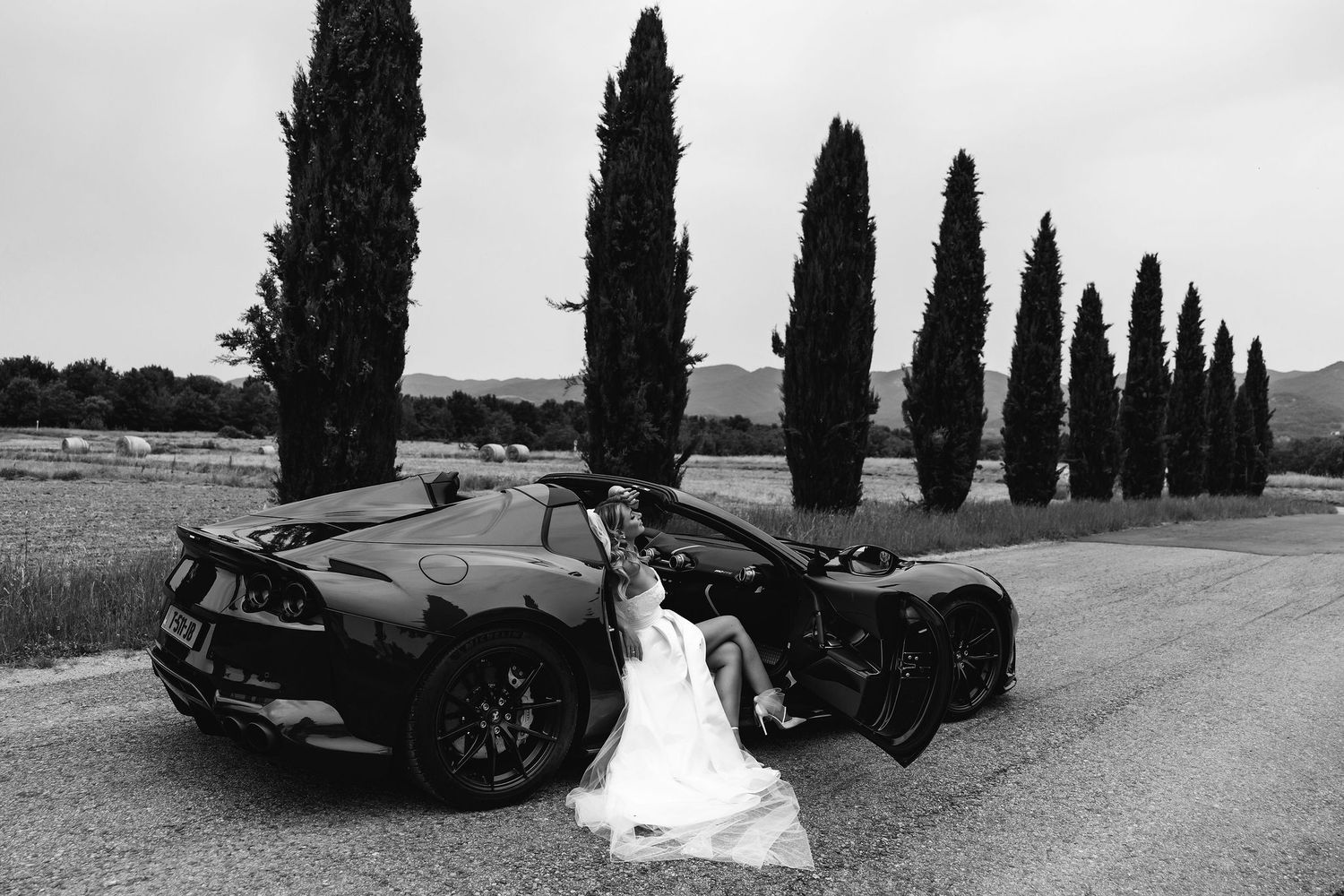 Dramatic black and white wedding photo with luxury cars and cypress trees.