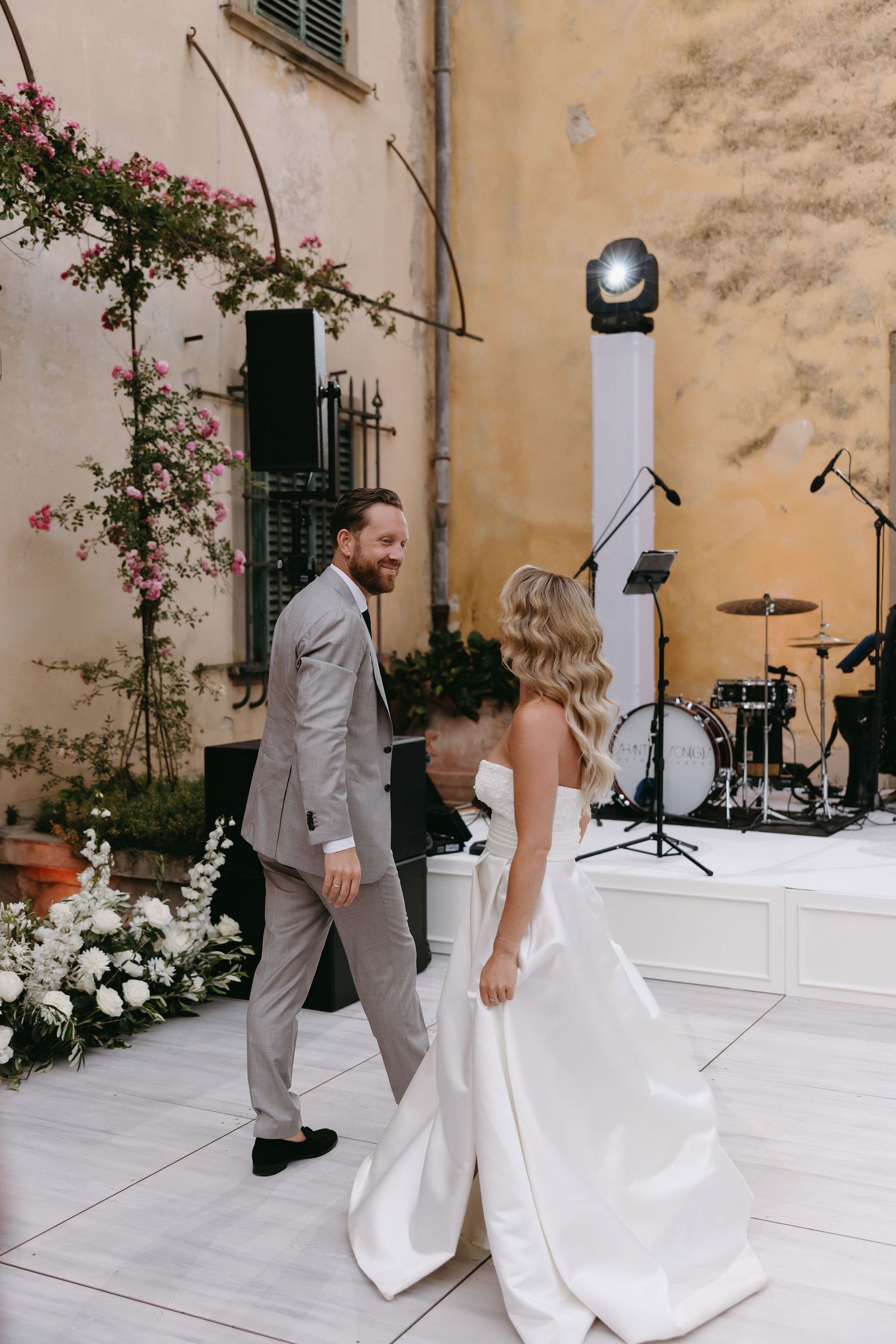 Wedding couple in formal attire standing near a stage setup with musical instruments.