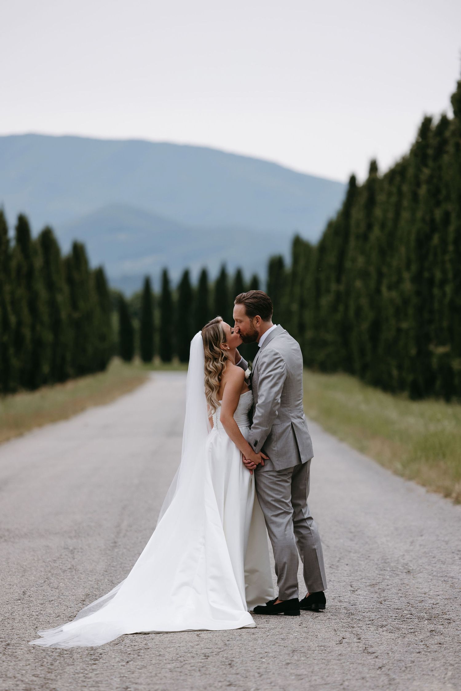 A romantic scene with a newlywed couple on a cypress tree-lined road in the mountains.
