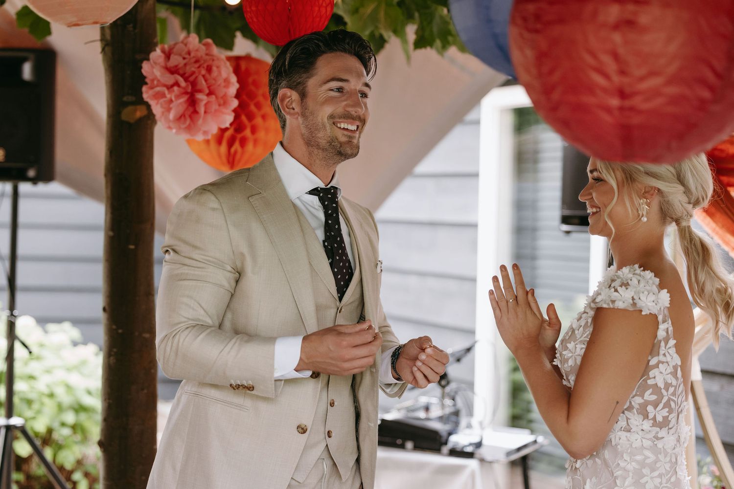 Joyful couple sharing a candid moment during their wedding ceremony under coral floral decorations.