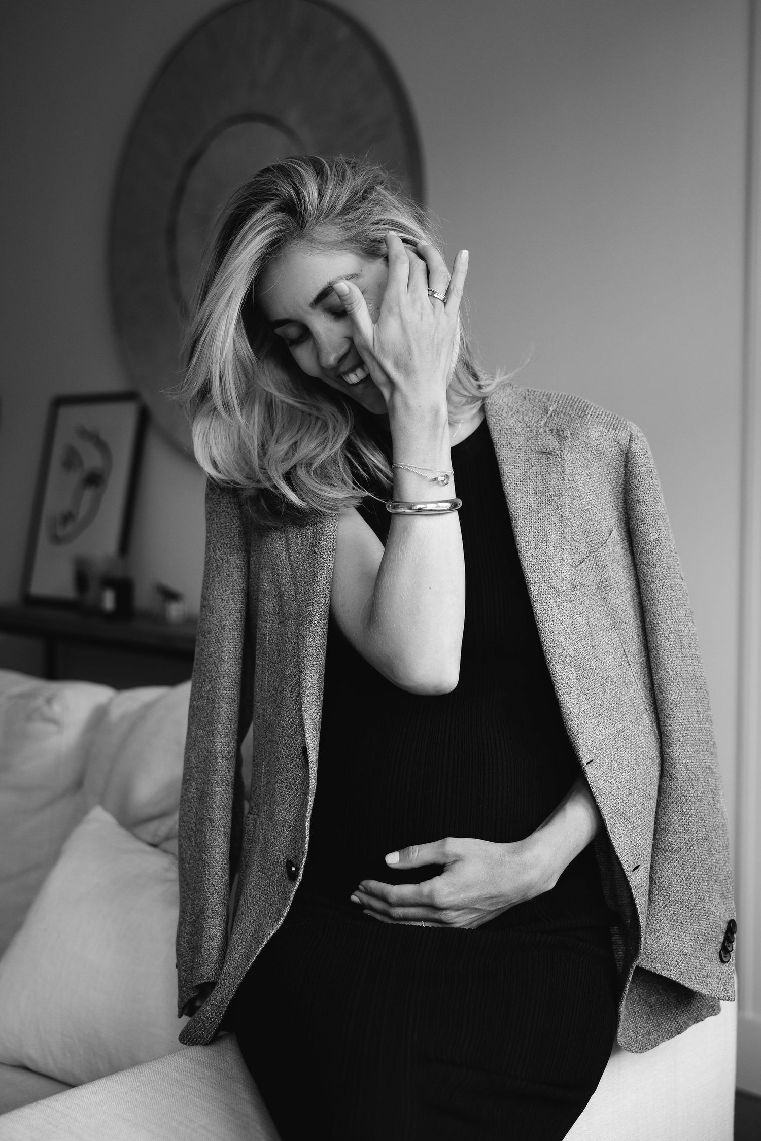 Black and white portrait of expectant mother in blazer touching forehead.