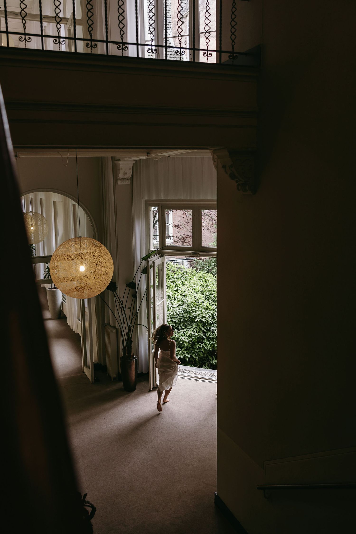 A silhouette figure walks through an elegant hallway with a hanging spherical pendant light and ornate architectural details.