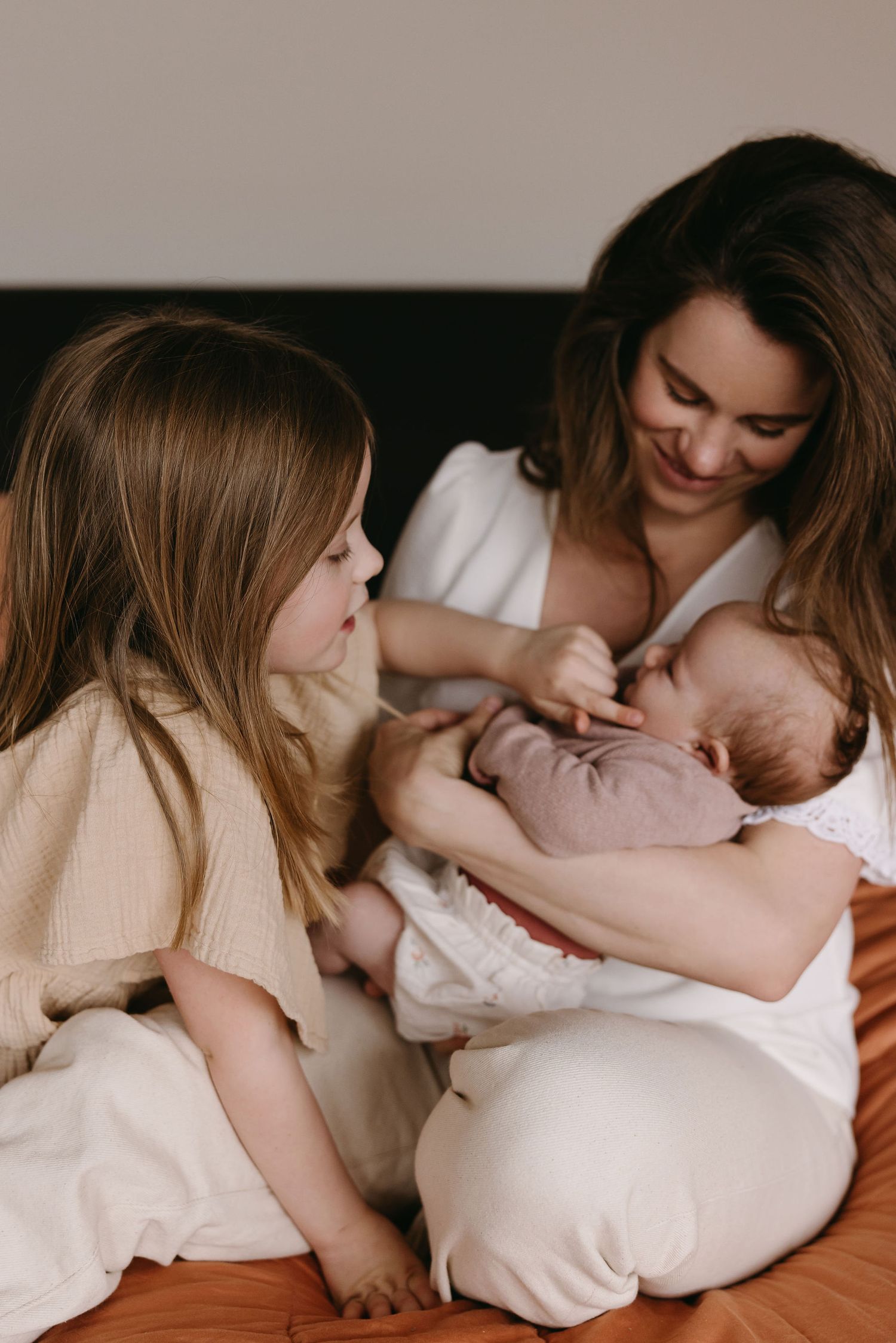 An intimate family scene showing a sweet moment with a newborn baby on soft white bedding.