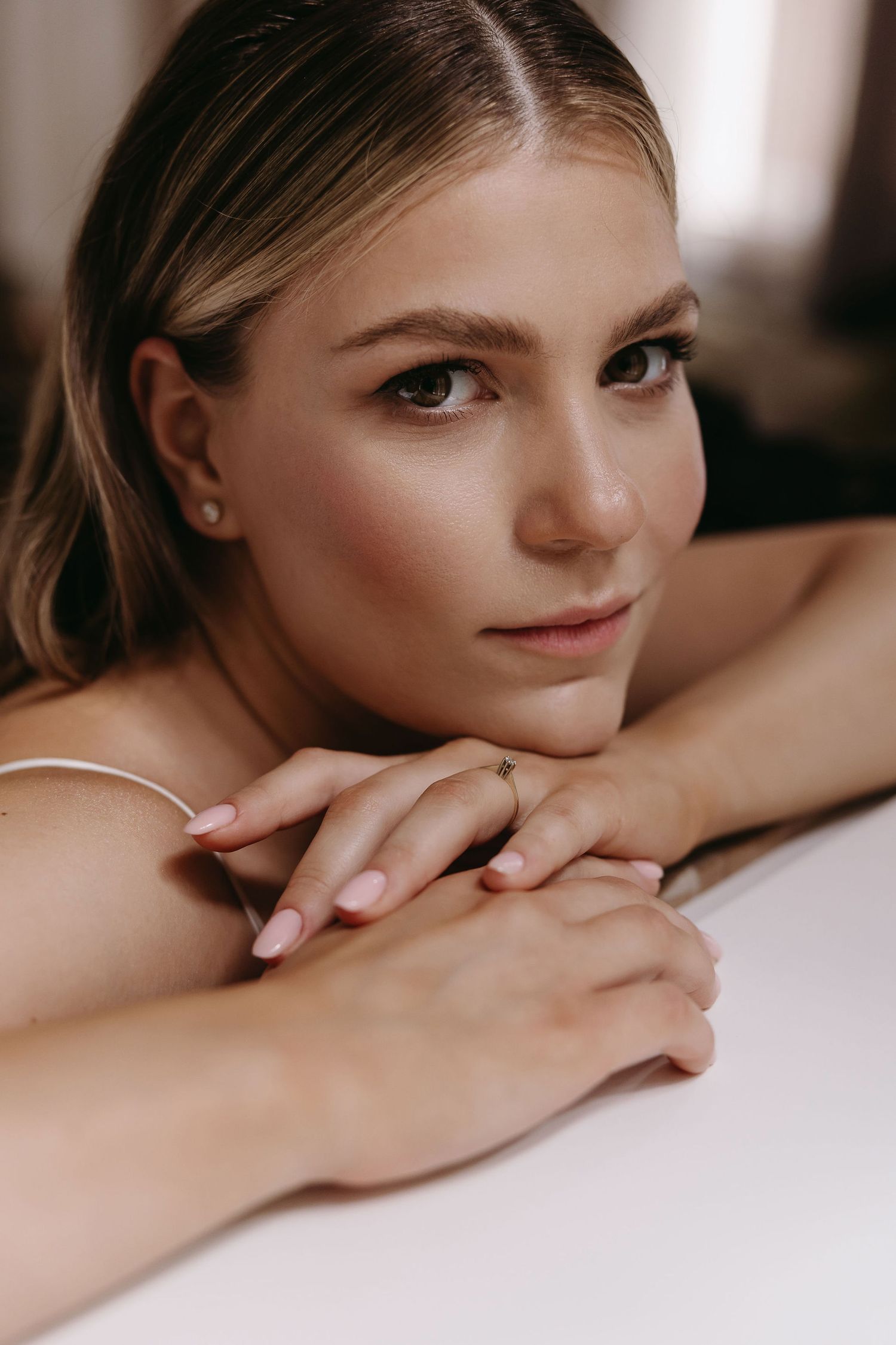 Close-up beauty portrait in soft natural lighting with neutral makeup and simple jewelry.