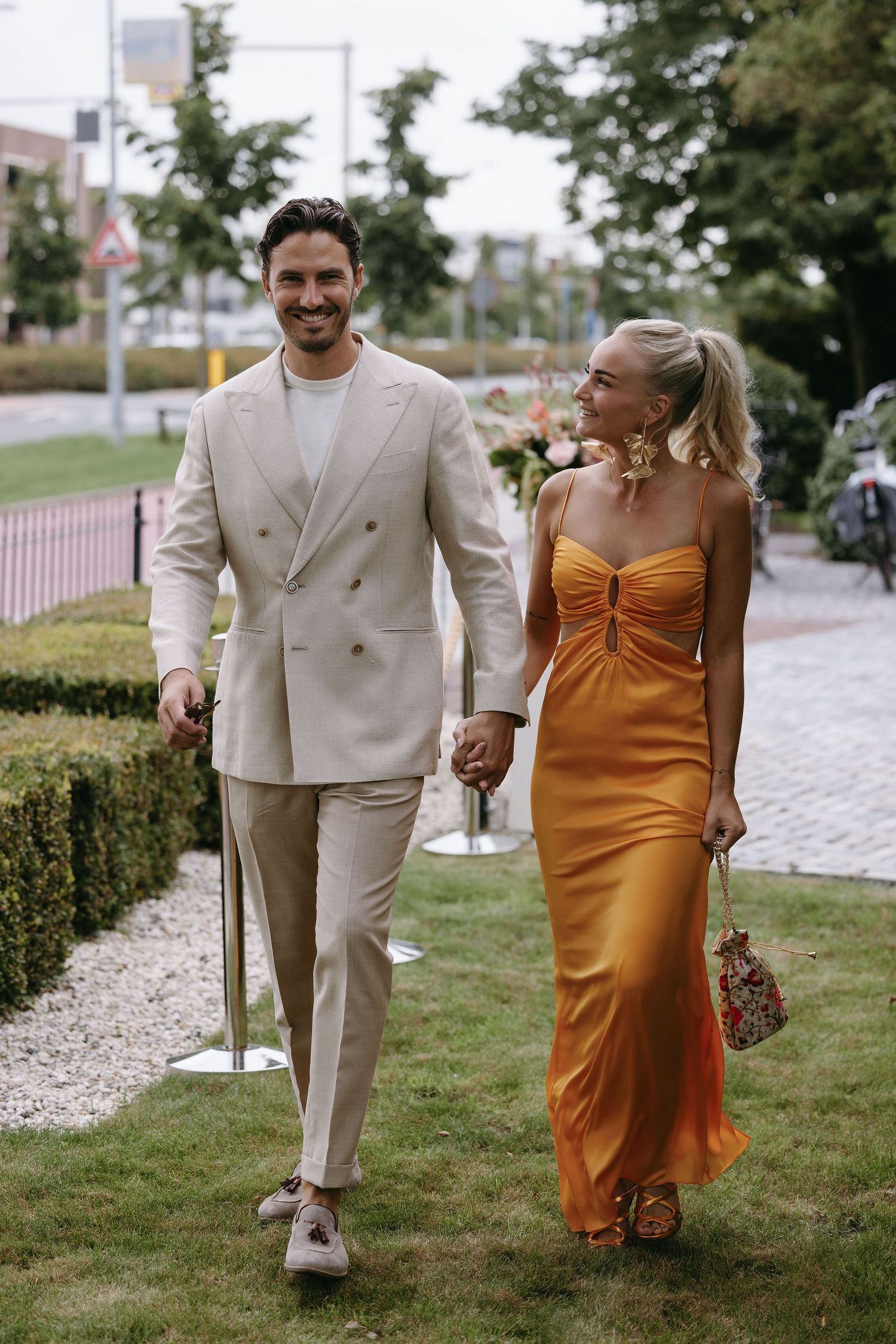 Couple walking along a stone path, wearing cream suit and orange formal dress.