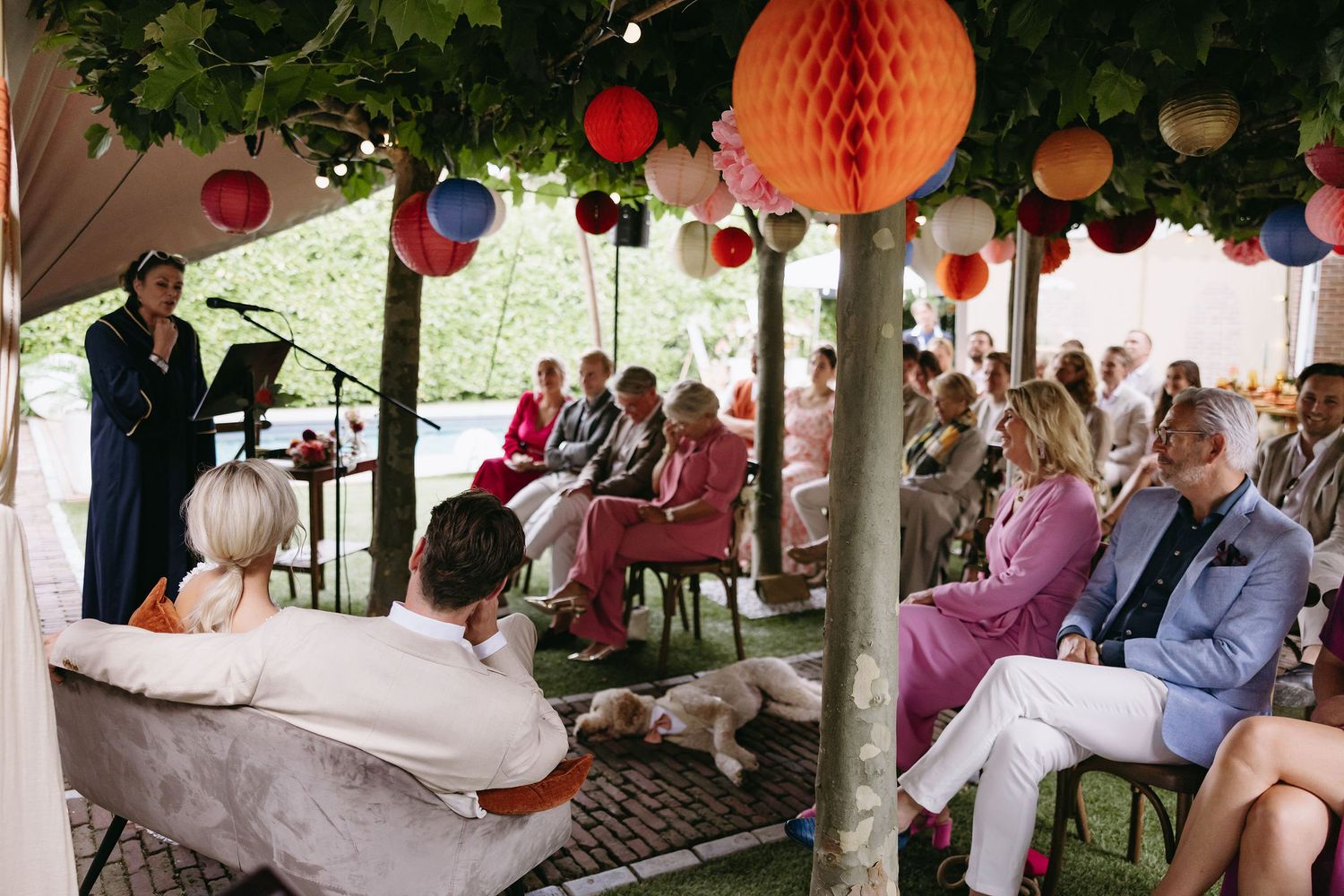 Wedding celebration under a tent with orange and red paper lantern decorations and guests seated at tables.