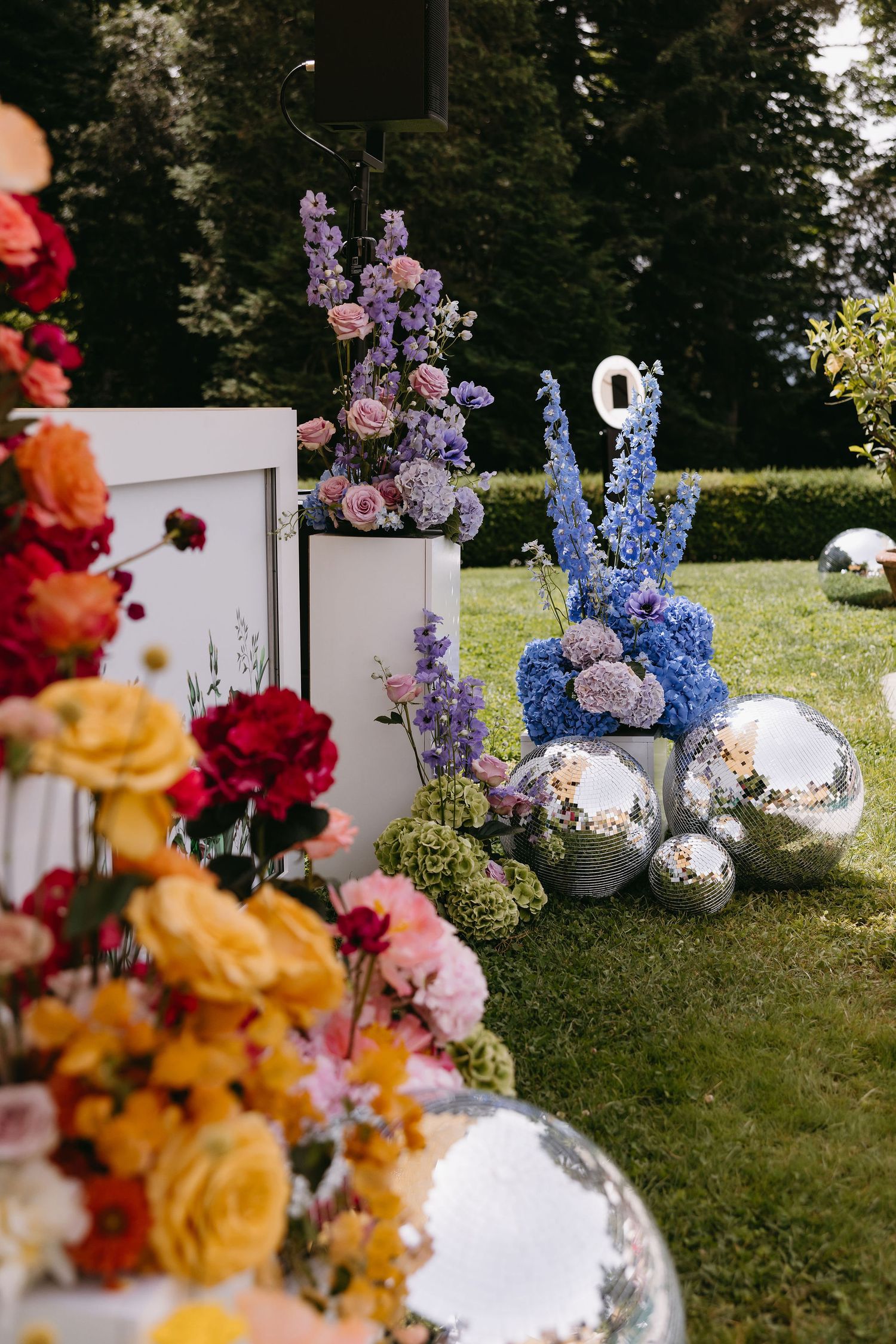 Elegant wedding decor featuring colorful floral arrangements with purple, blue, and orange flowers alongside mirrored disco balls on grass.
