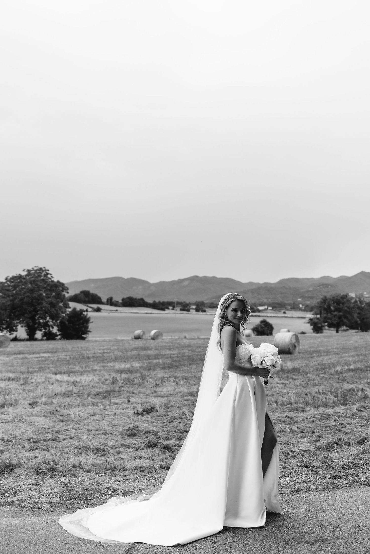 Black and white landscape photo of a couple in wedding attire embracing in an open field.