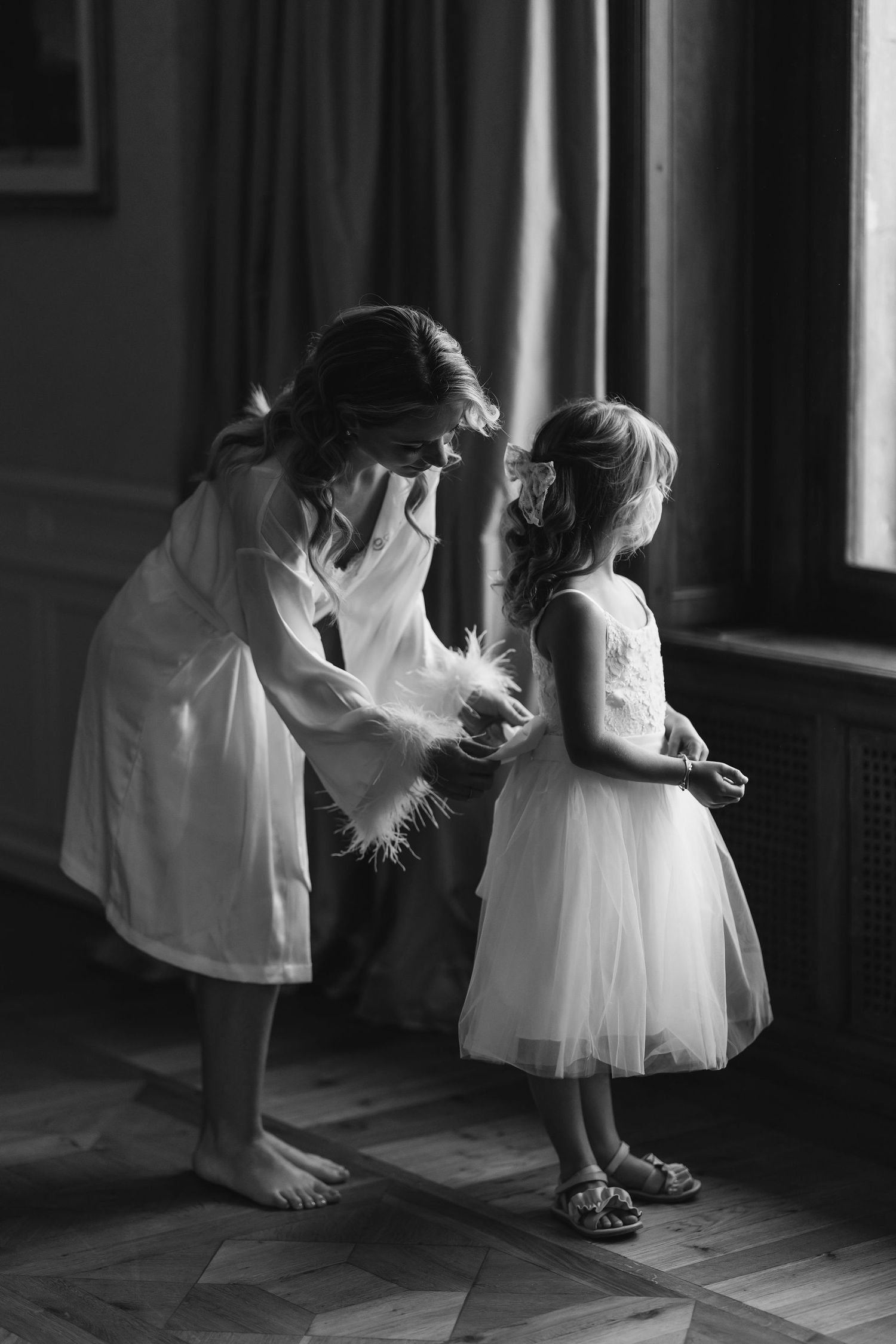 A tender moment captured in black and white as two figures interact near a window.
