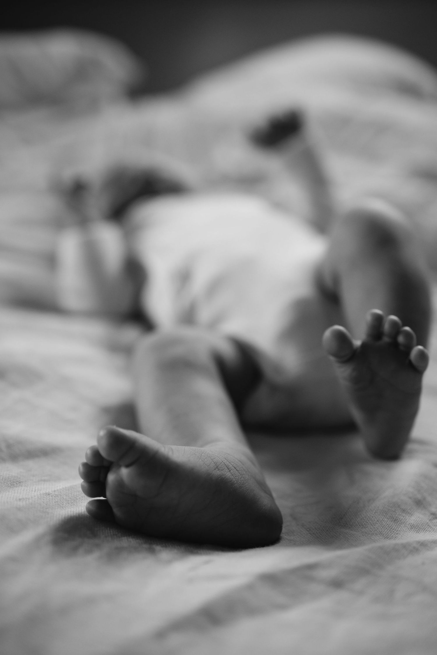 Close-up black and white images of tiny feet resting on soft bedding.