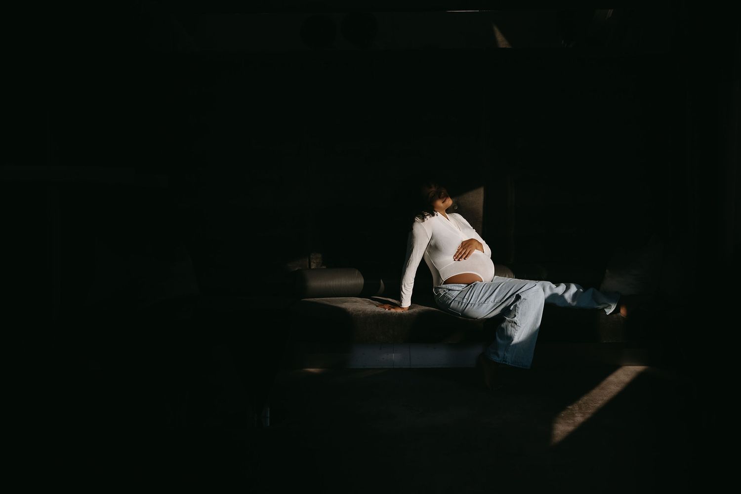 Dark artistic photograph with minimal lighting showing a reclining figure.