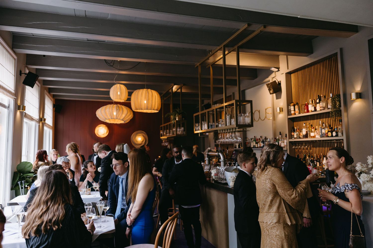 Wedding reception venue with hanging lanterns and guests mingling at a dimly lit bar.