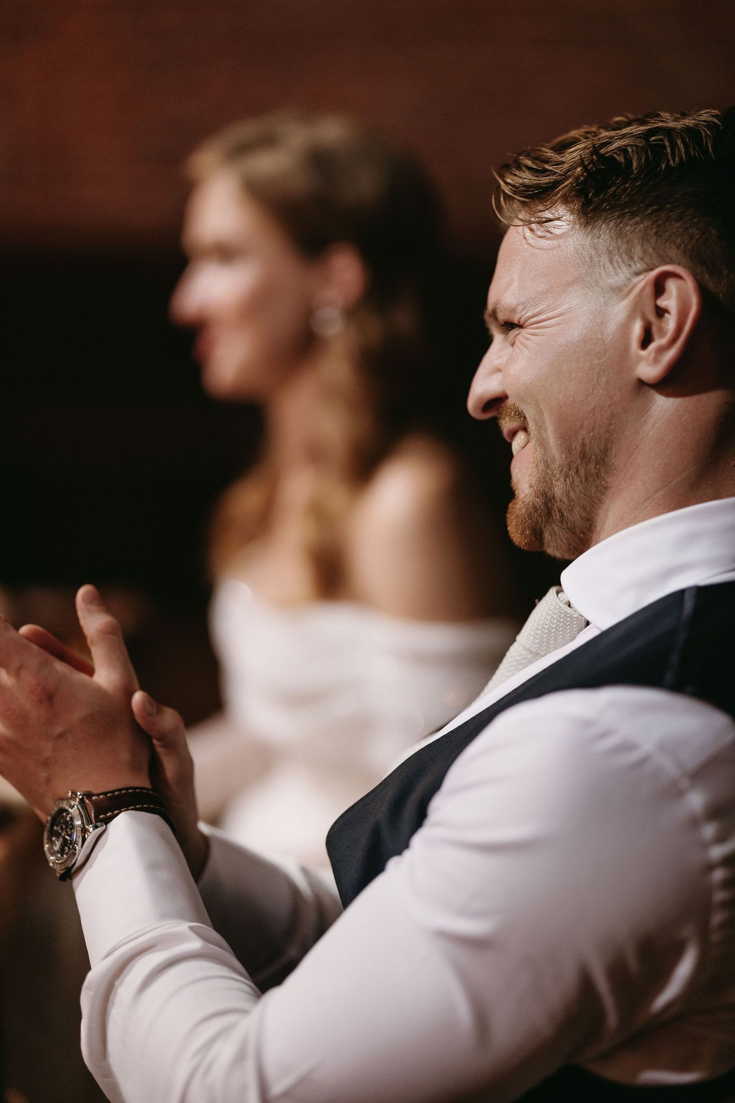 A candid reception moment showing expressions of joy and laughter during wedding speeches.