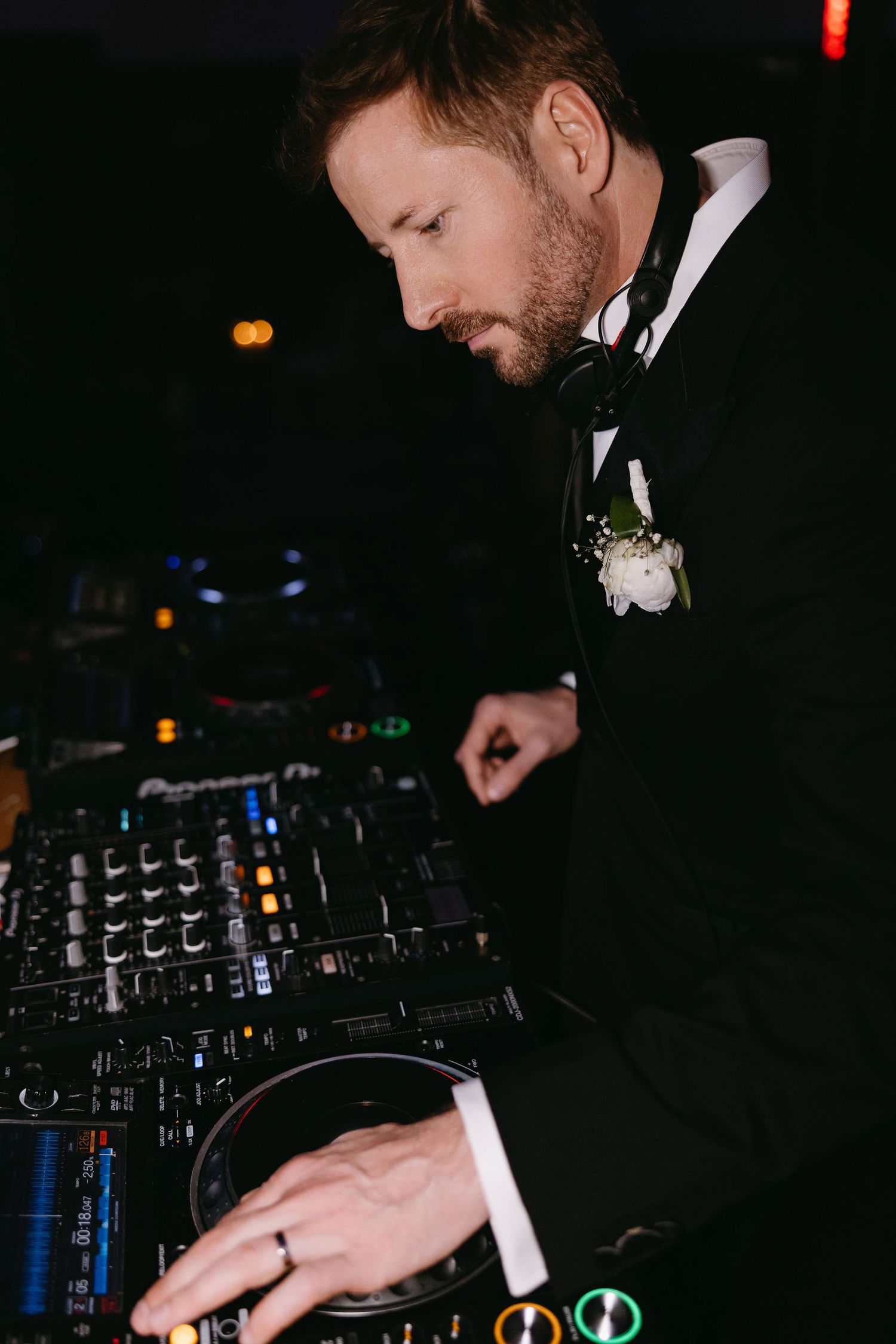 Wedding DJ in formal attire working professional equipment in dark venue setting.
