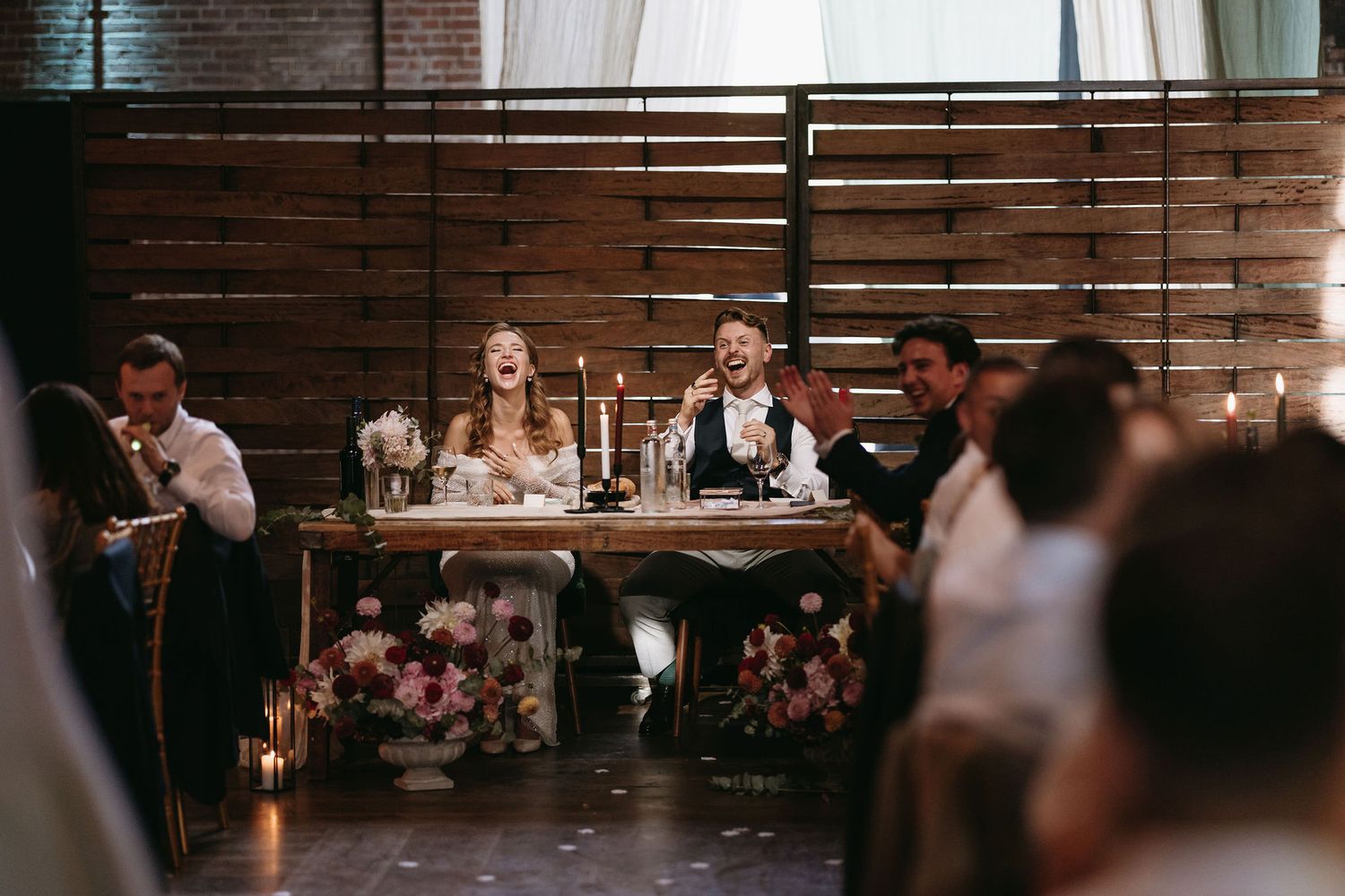 Wedding reception venue features exposed brick walls with floral arrangements and string lights creating ambiance.
