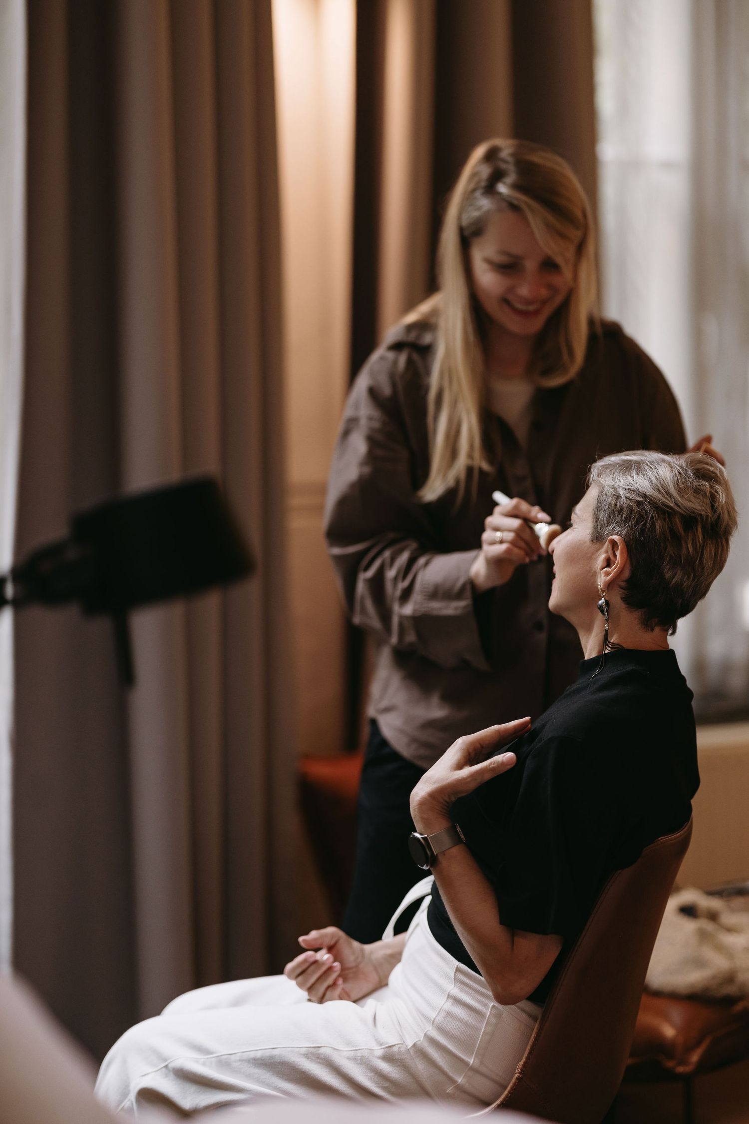 A makeup artist applies cosmetics to someone seated in a chair during wedding preparations.