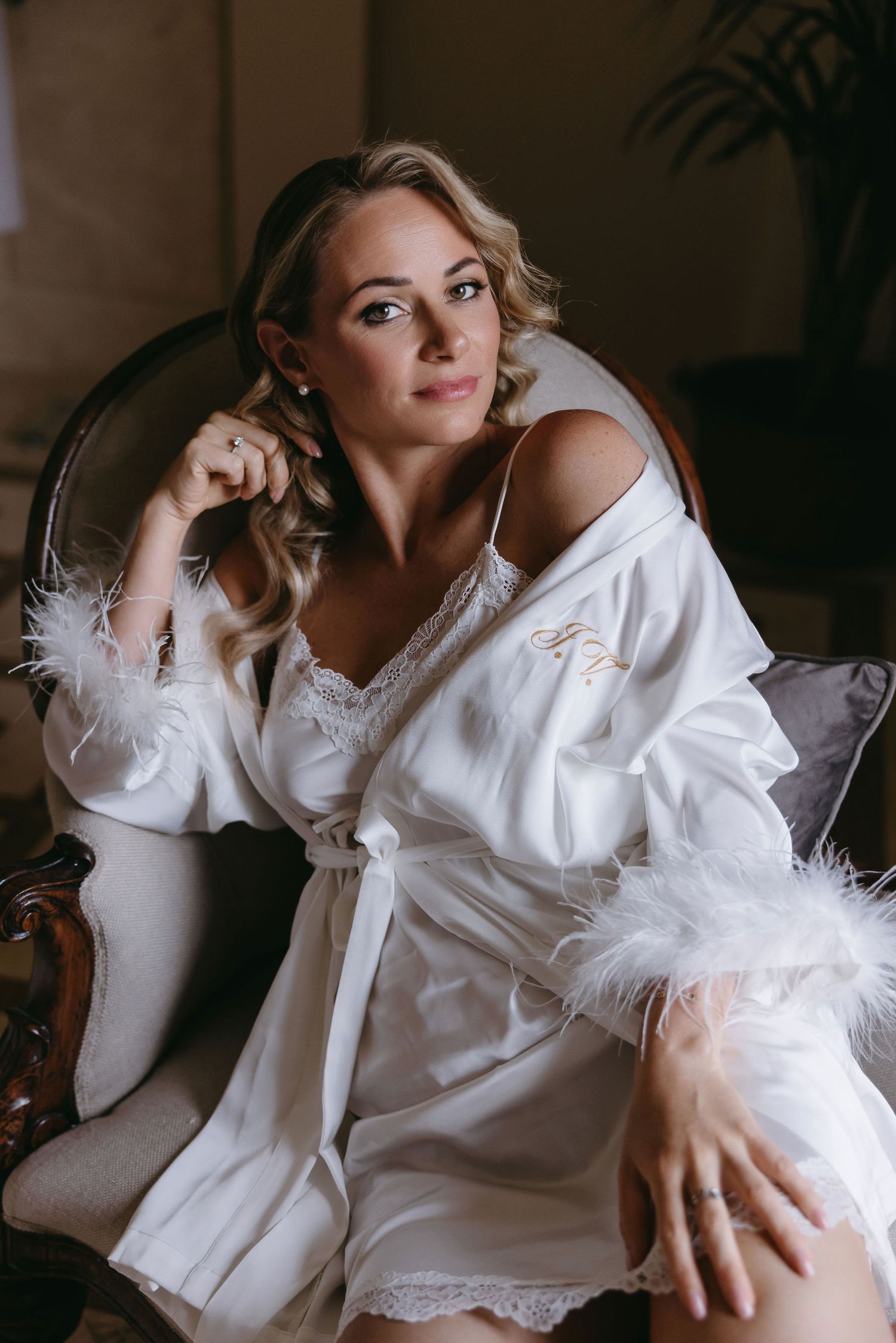 A person in white feathered robe lounges on an elegant chair during wedding preparations.